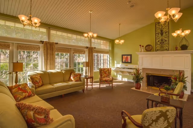 Sunlit common living room with sofas, armchairs, a fireplace and large windows.