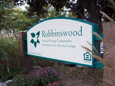 An exterior entrance sign for Robbinswood Assisted Living Community with landscaped surroundings.