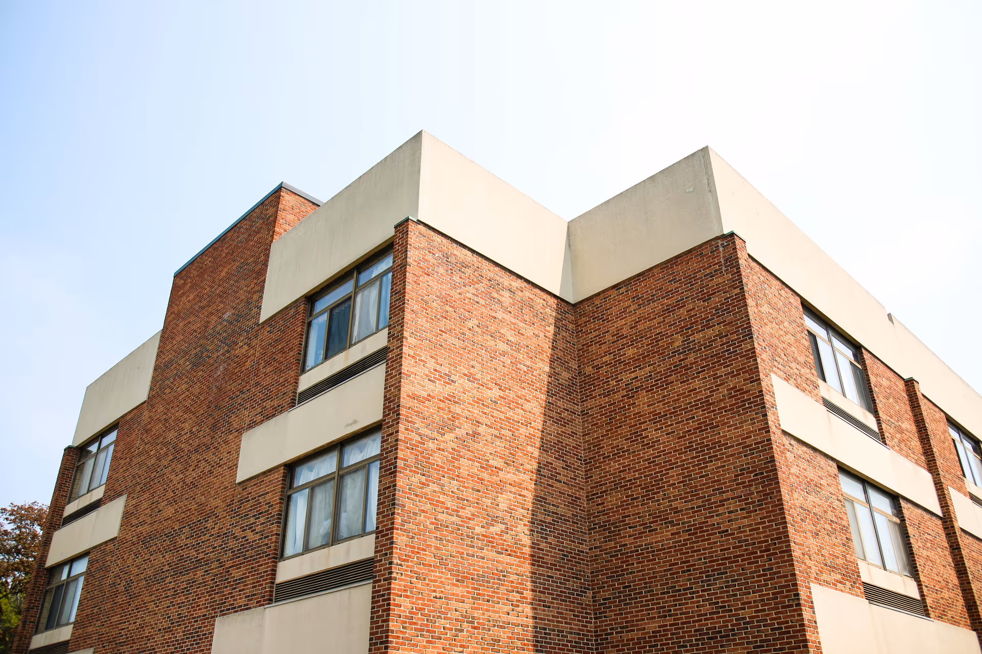 Exterior view of a multi-story brick building with several windows and beige concrete accents under a clear sky.