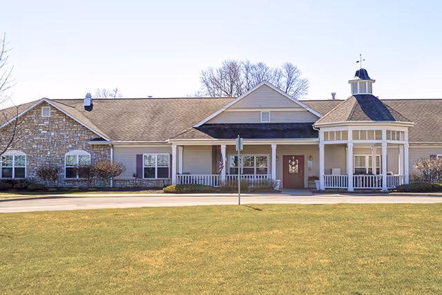 Single-story senior living facility facade with porch, flag, and well-kept front lawn.