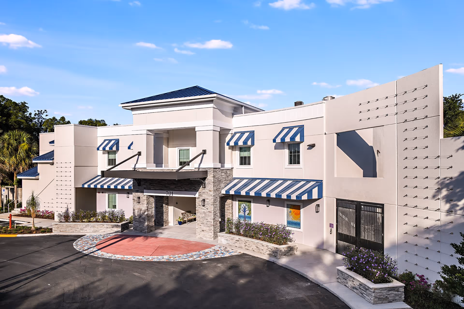 Front entrance of a two-story senior living facility with striped awnings, stone portico and a circular driveway.