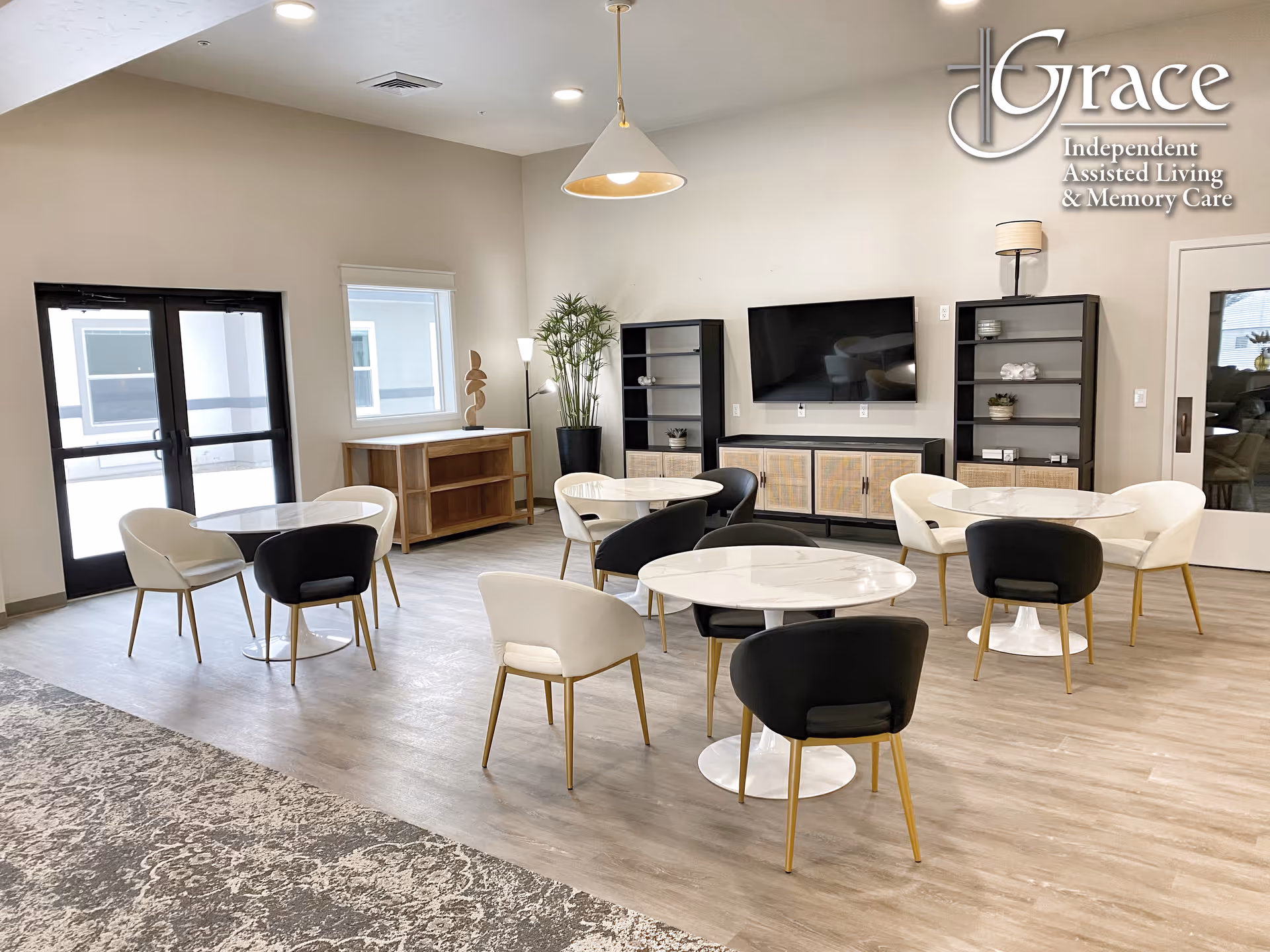Bright lobby lounge with round marble tables, white and black chairs, and a wall TV.
