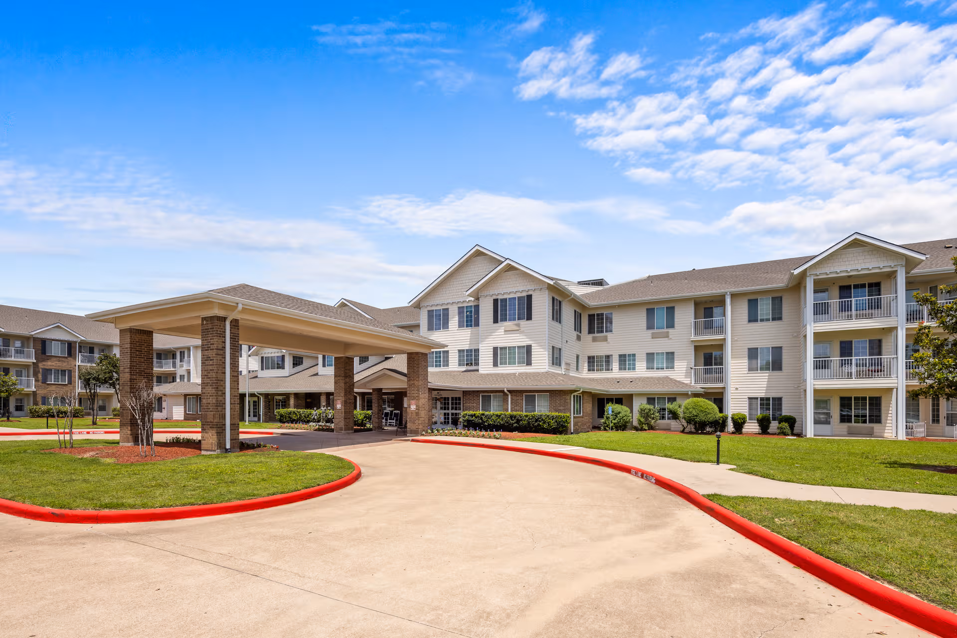 A multi-story senior living facility exterior with a covered entrance and manicured lawn.