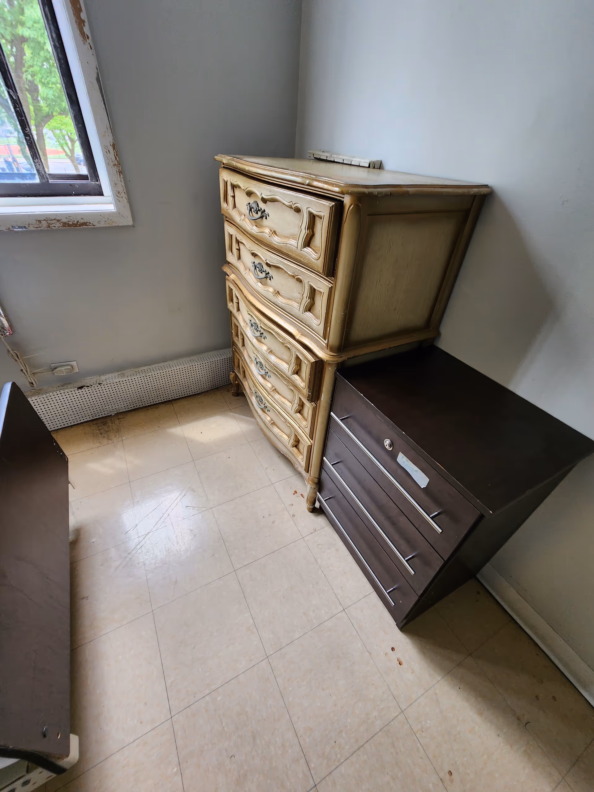 Corner of a room with a vintage beige dresser beside a dark brown chest.