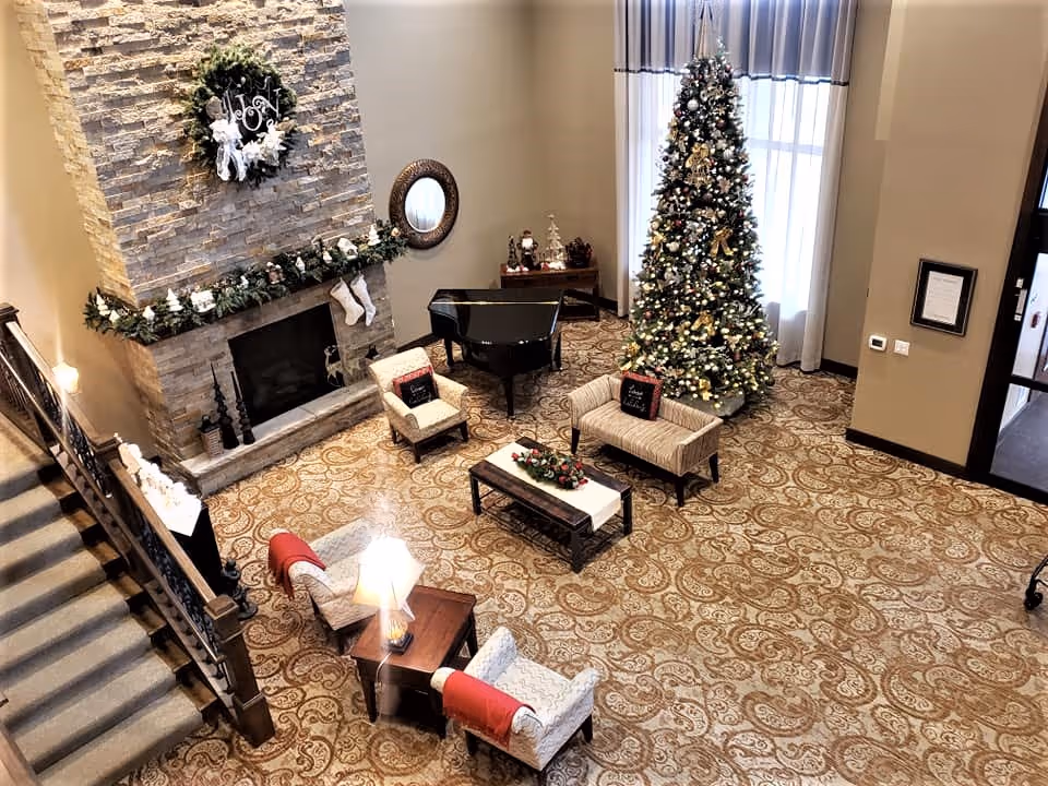 View from above of a decorated lounge with a fireplace, grand piano, seating area, and a large Christmas tree.