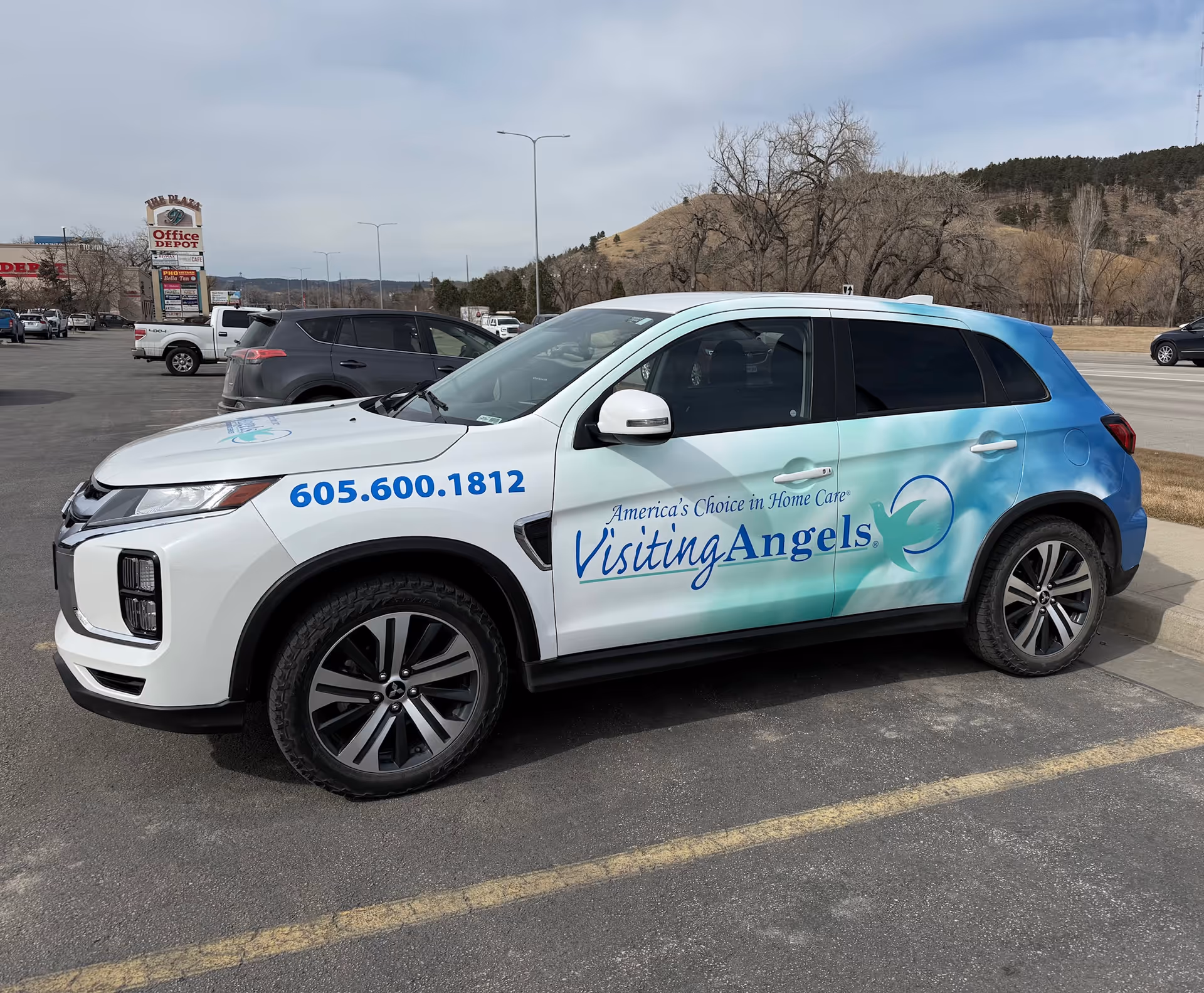 Visiting Angels branded SUV parked in a lot, with hills in the background.
