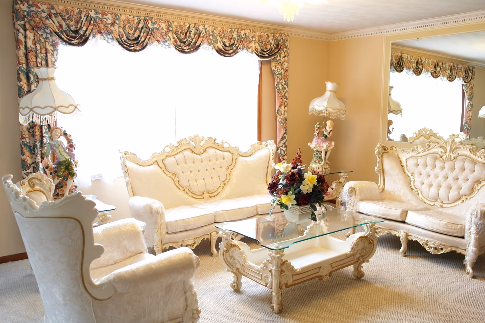 Elegant cream-colored living room with ornate sofas, glass coffee table, and floral centerpiece.