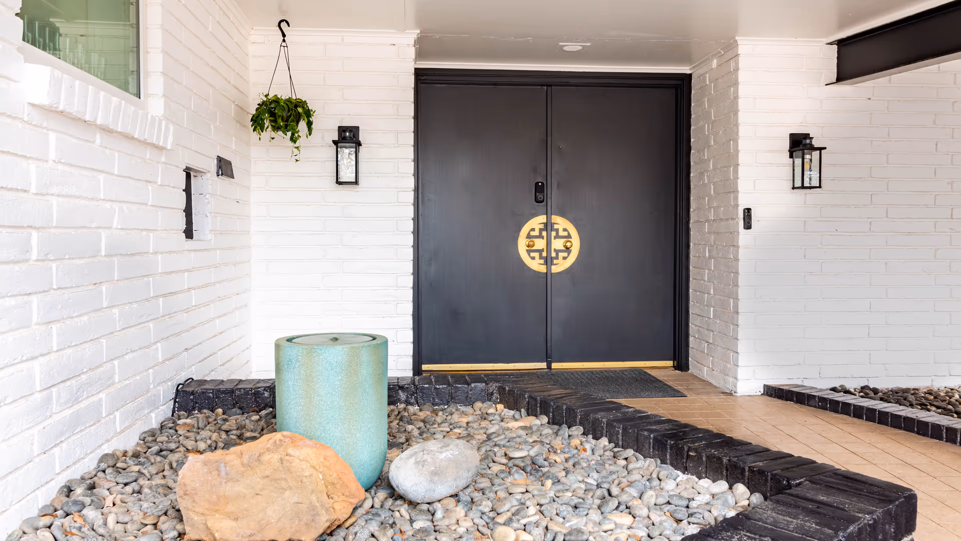 Dark double doors with gold emblem, flanked by white brick exterior and pebble landscaping.