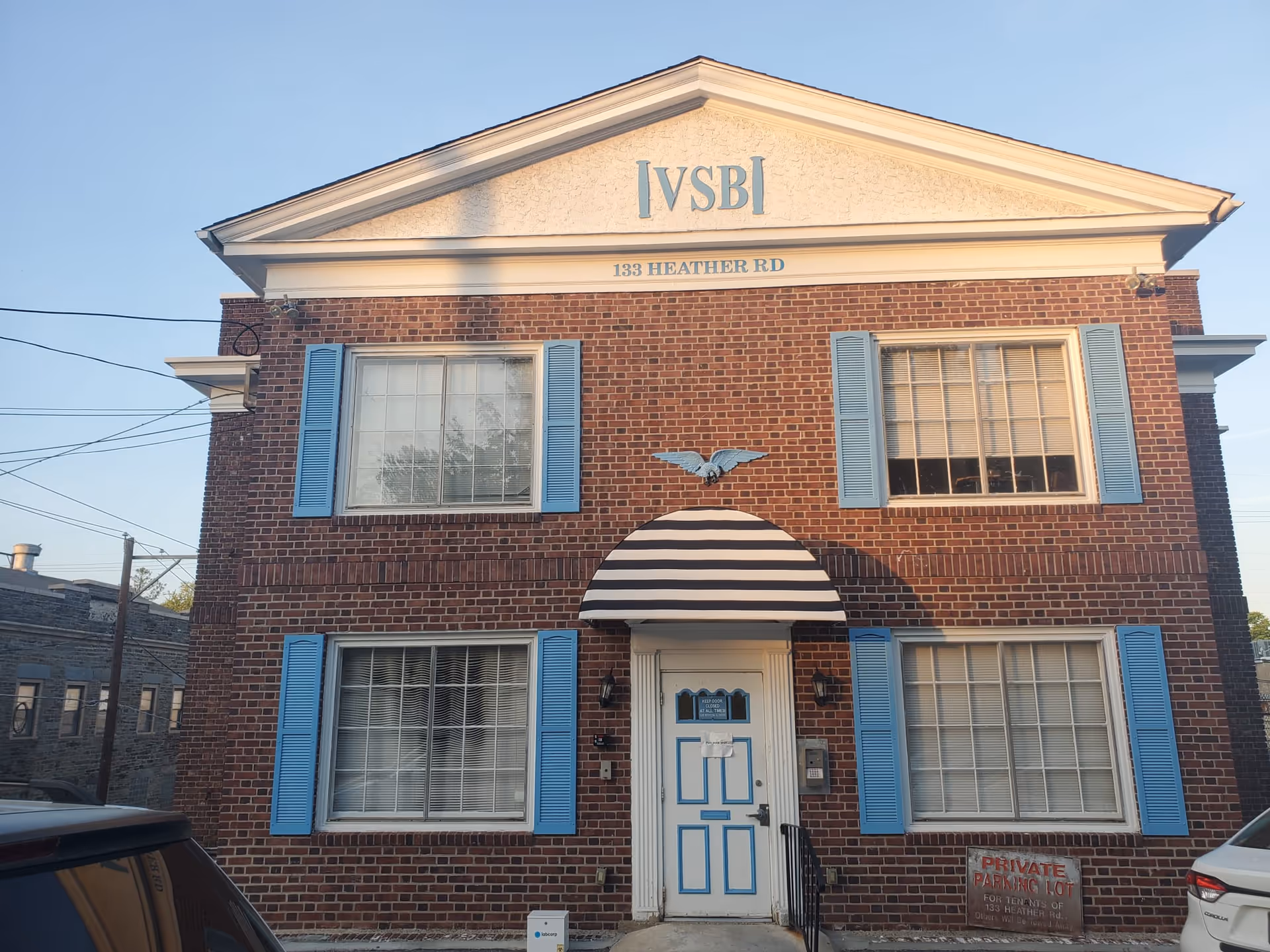 Brick two-story building with blue shutters and striped awning over white entrance.