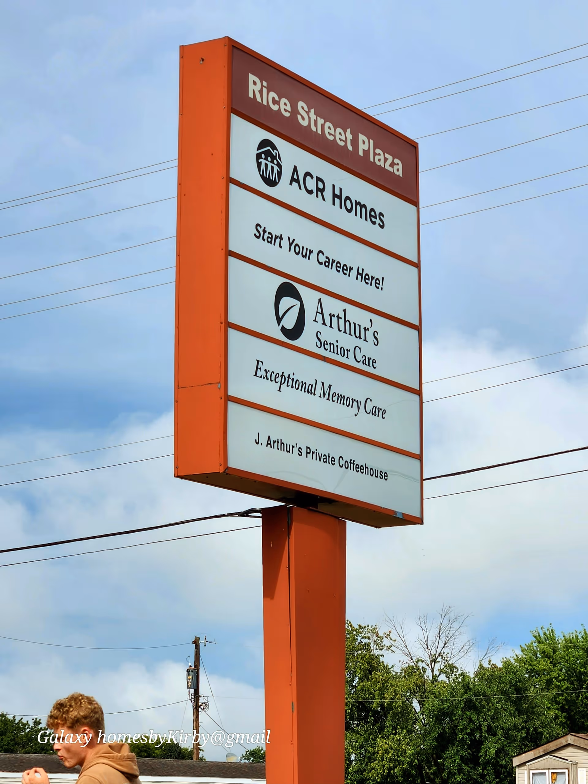 Tall orange signboard outside Rice Street Plaza advertising ACR Homes against a blue sky