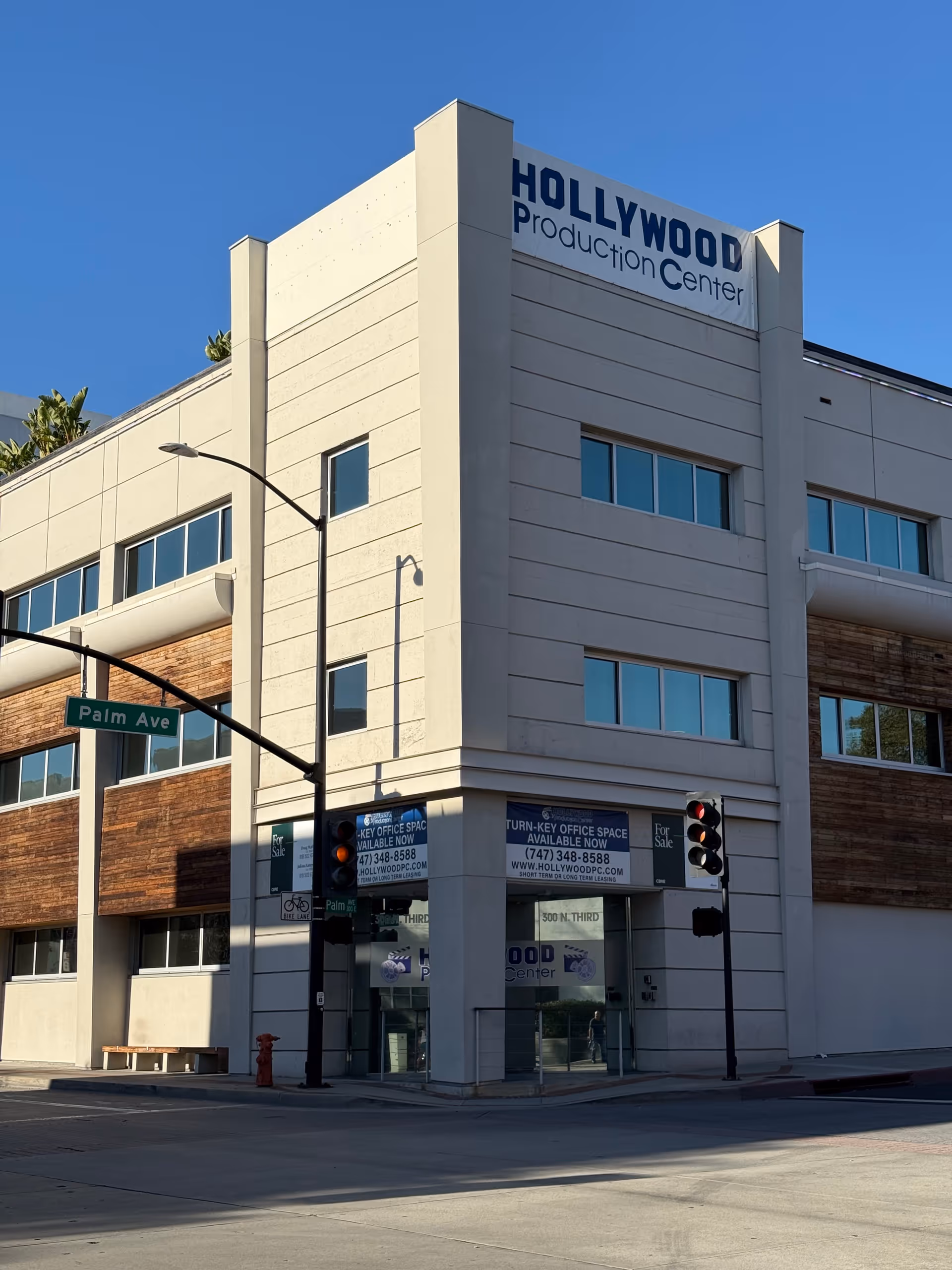 A modern beige office building at a street corner with a Palm Ave sign.