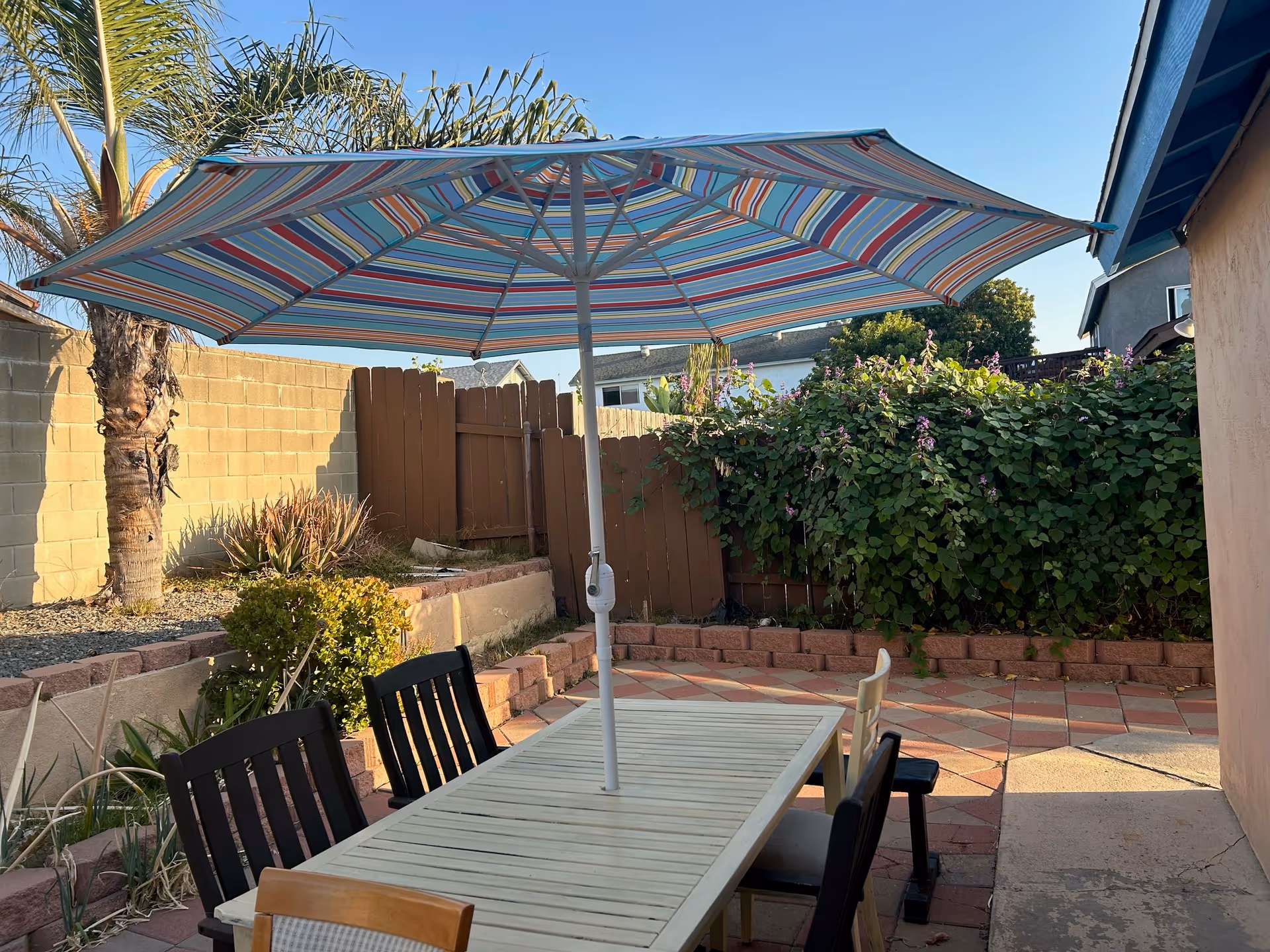 Outdoor patio with striped umbrella, table, chairs, and surrounding plants.