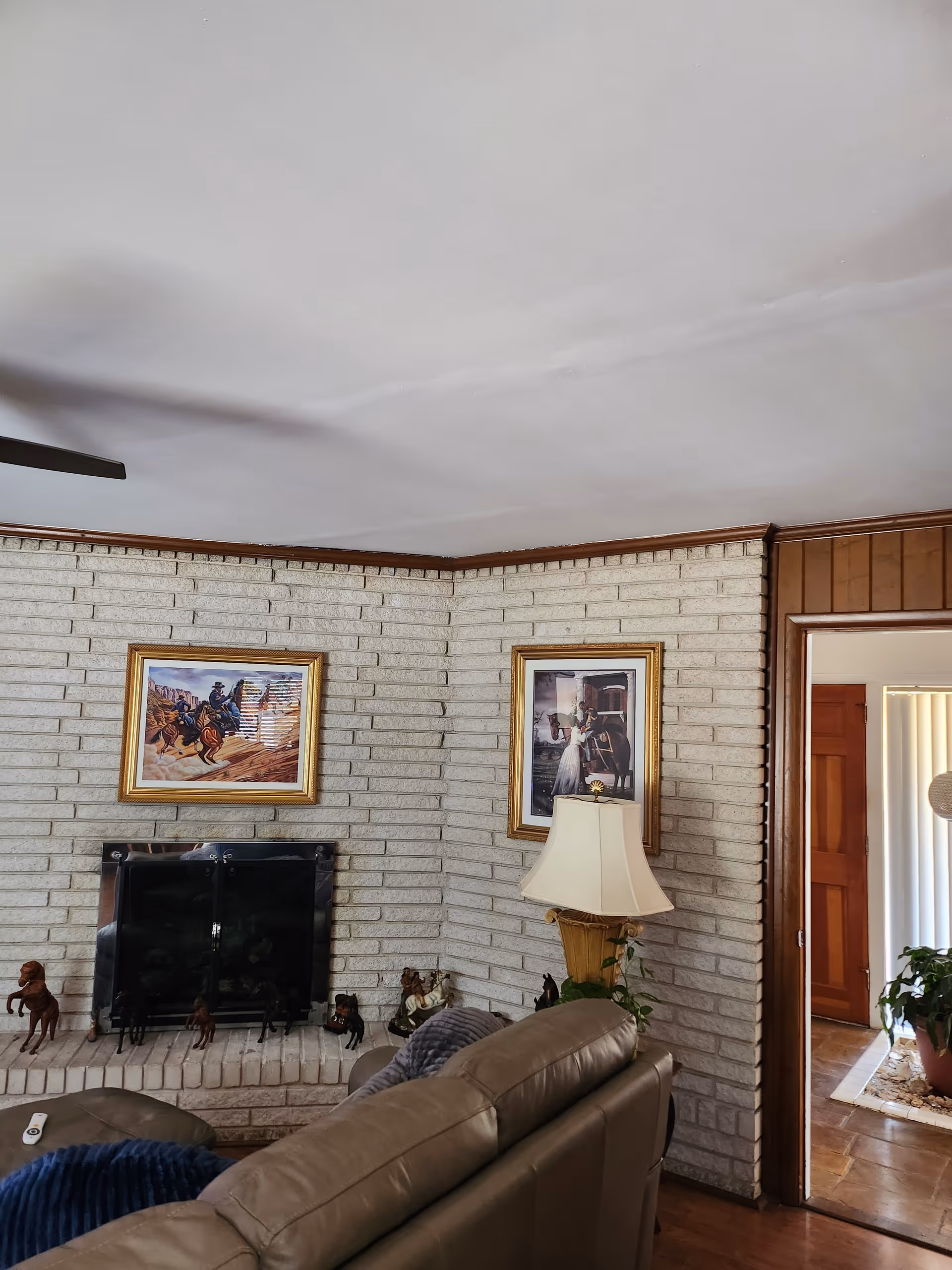Cozy living room with brick fireplace, framed art, leather sofa, and decorative plants.