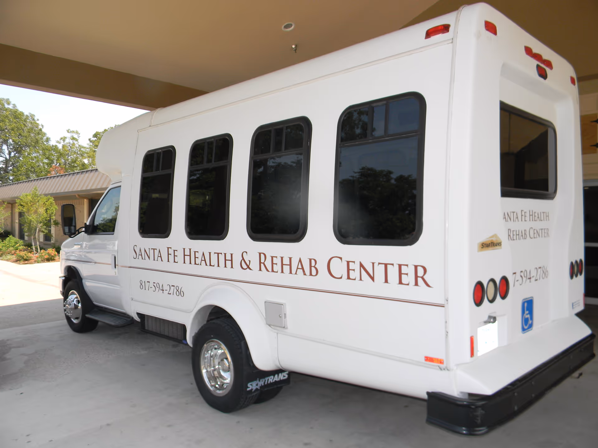 White shuttle bus with Santa Fe Health & Rehab Center lettering parked beside a building.