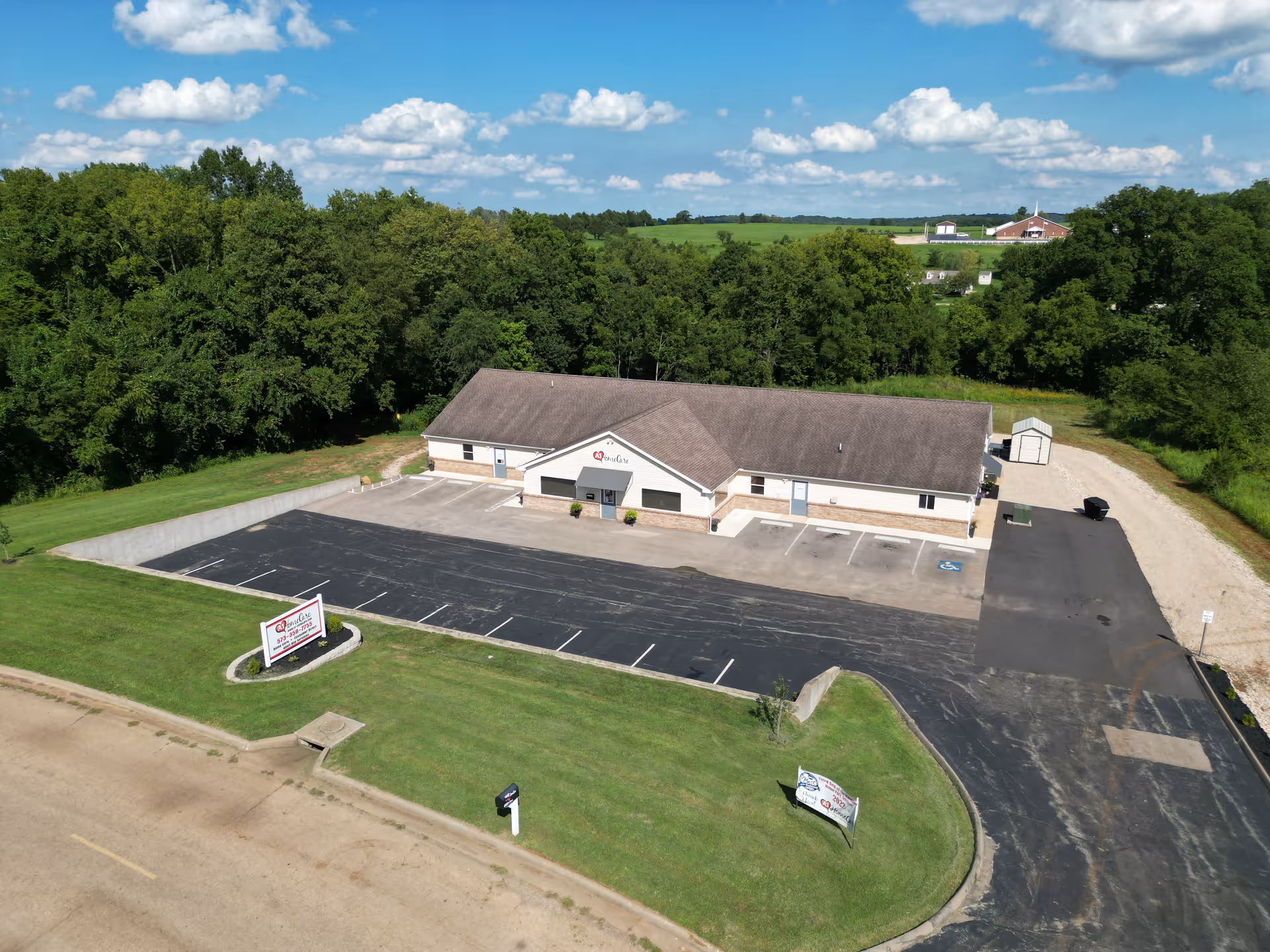 Aerial view of a single-story care facility with expansive parking, surrounding trees, and rural landscape.