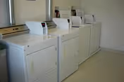Row of washing machines in a bright senior facility laundry room.