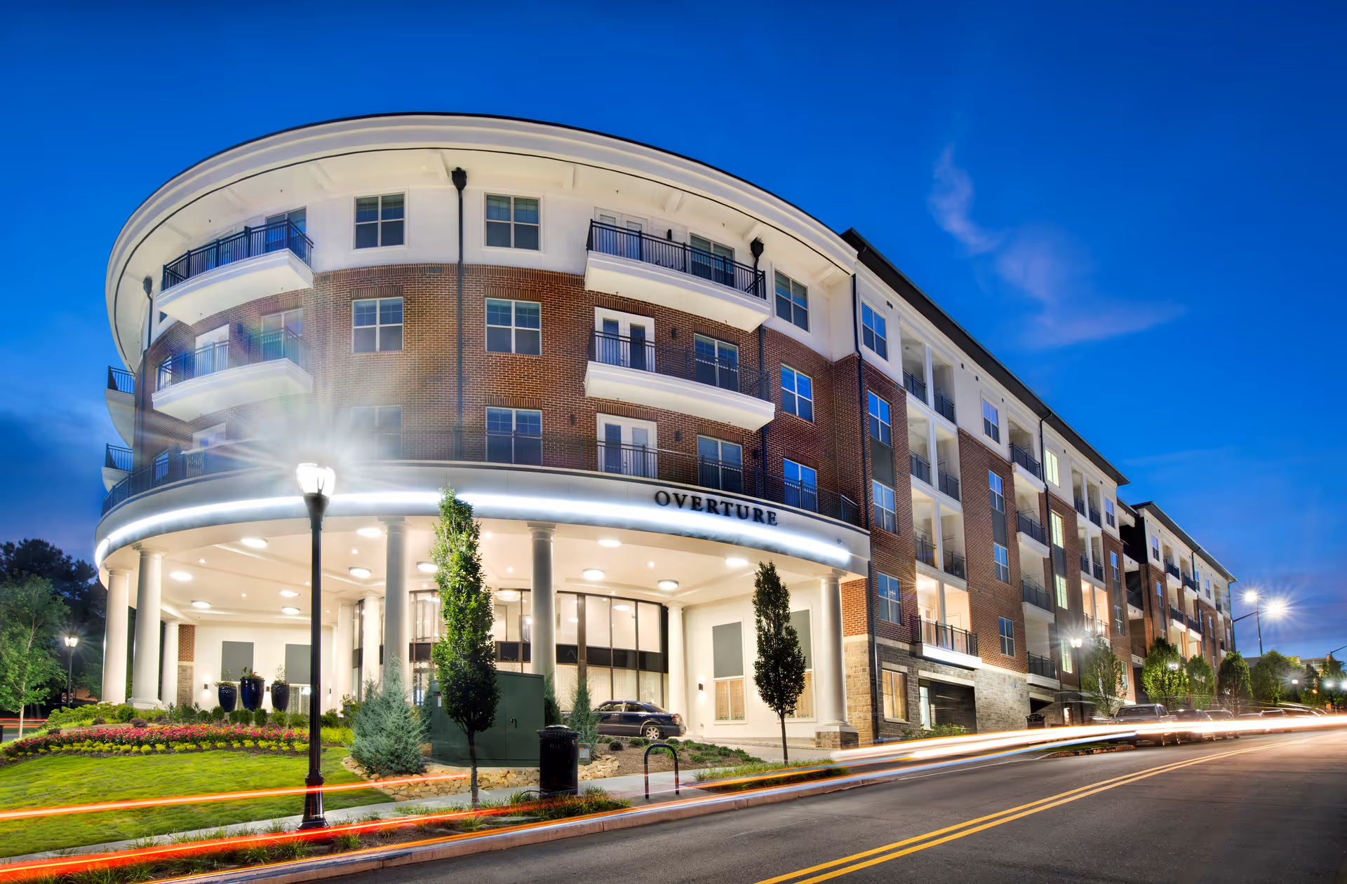 Curved brick senior living building with illuminated entrance at dusk, Overture Buckhead South.