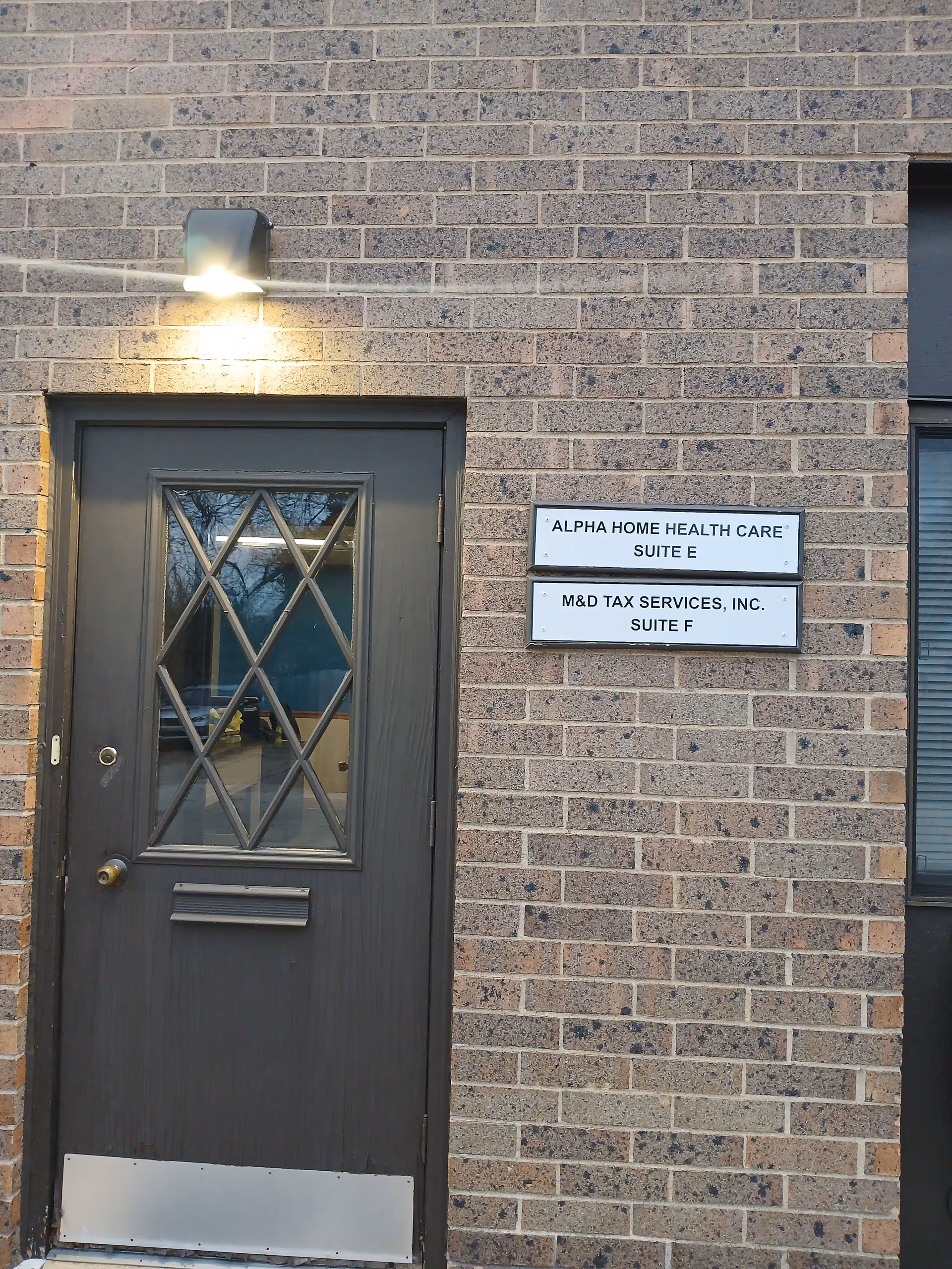 Exterior brick building with a dark front door, light above, and two signs on the wall.
