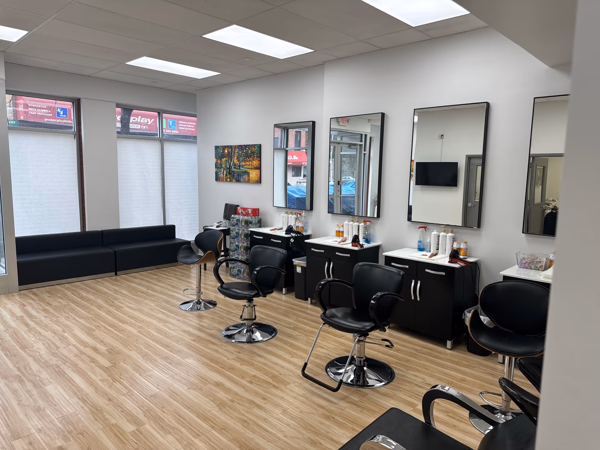 Modern salon area with black styling chairs, mirrors, and service cabinets along a bright interior.