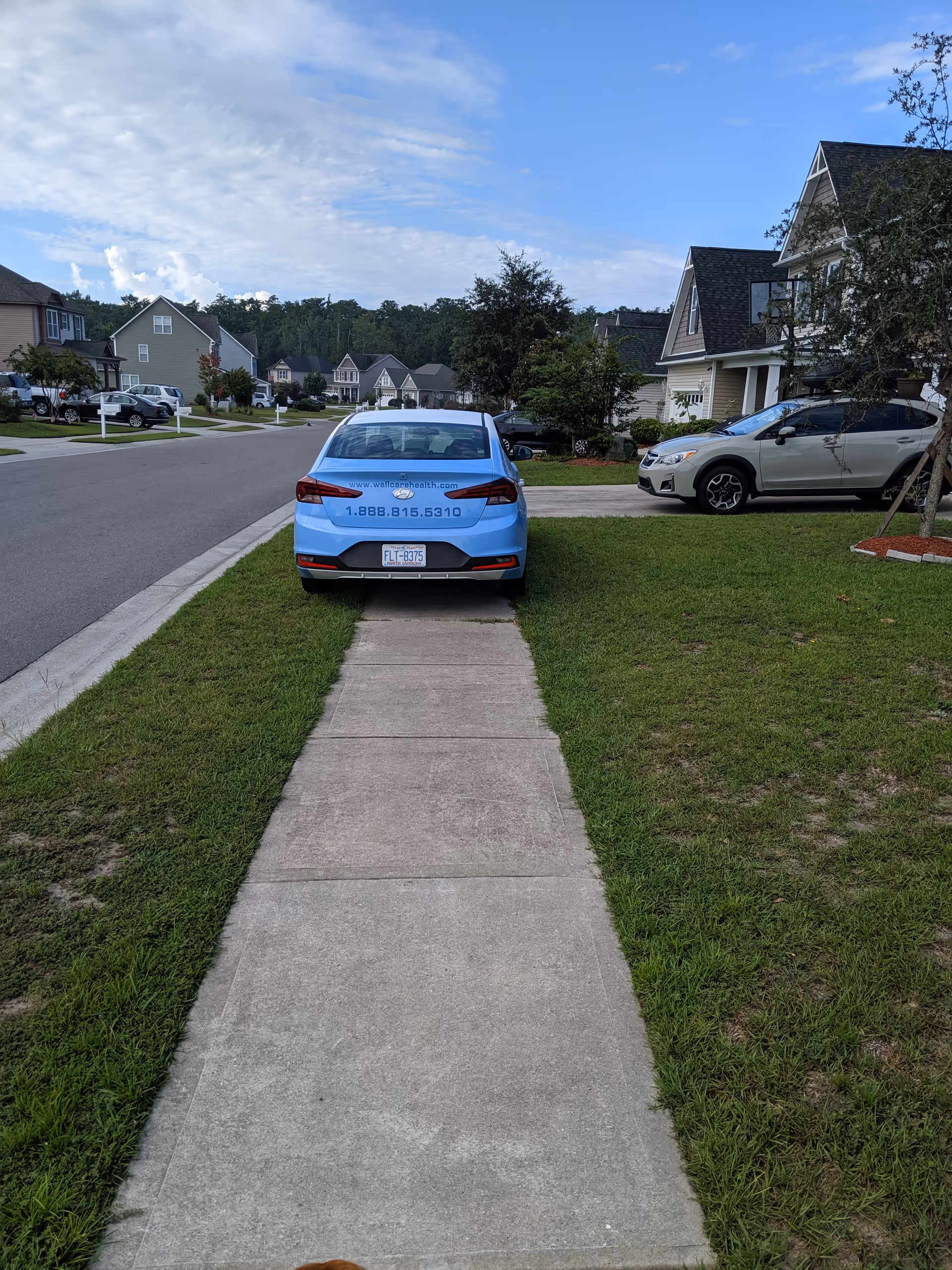 Blue car with Well Care Health contact info parked on a residential street.