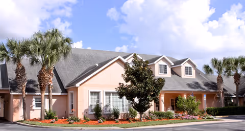 Exterior view of a peach-colored senior living facility with palm trees and clear blue sky.