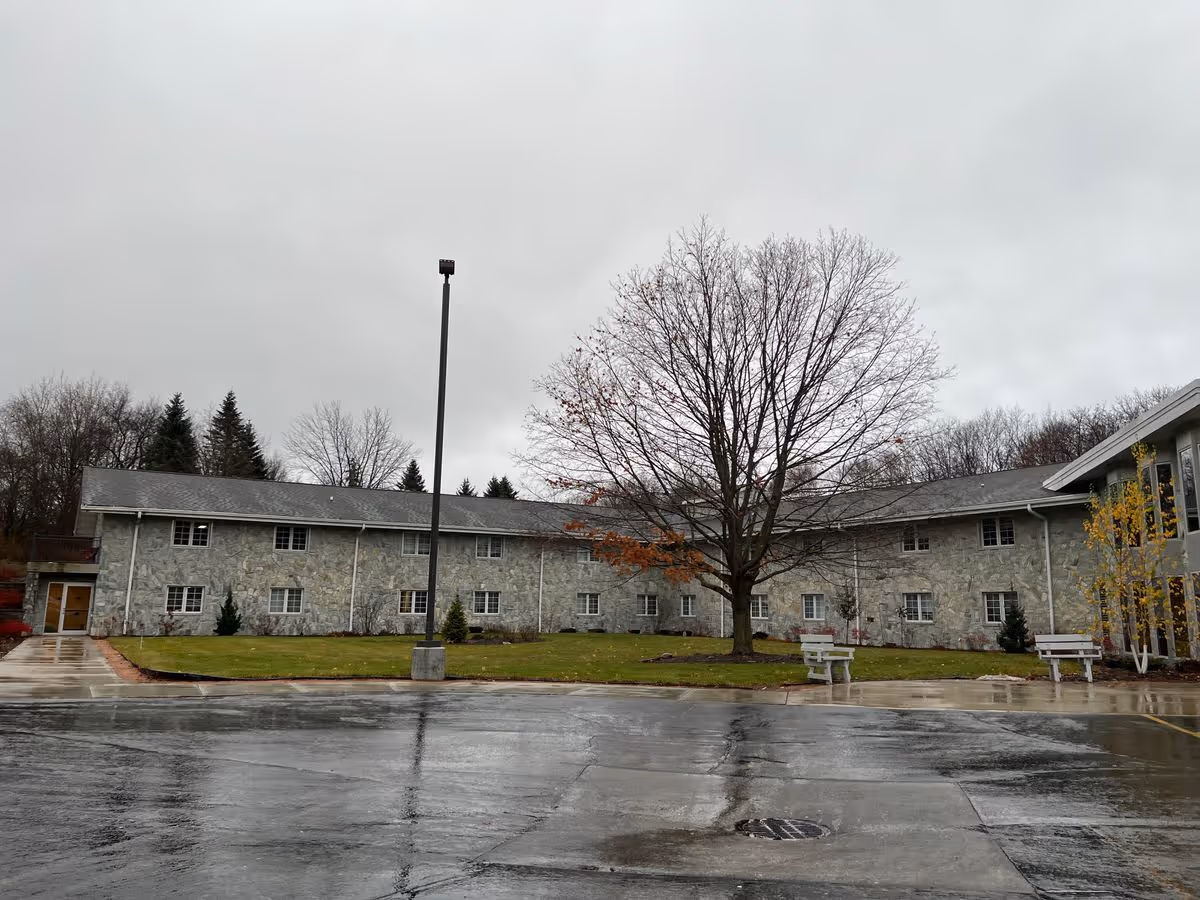 Two-story stone-faced building with a large leafless tree and wet parking lot in front.