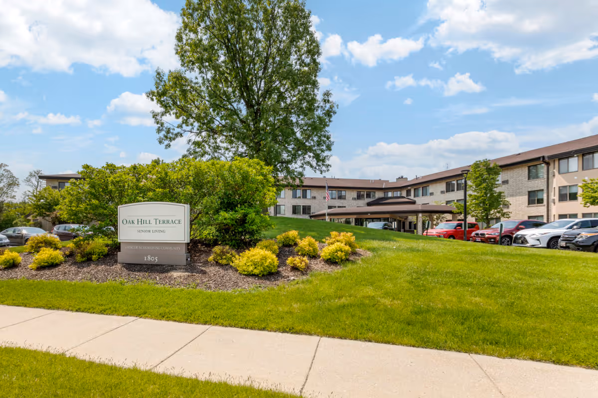 Oak Hill Terrace Senior Living exterior front with sign, lawn, and parked cars.
