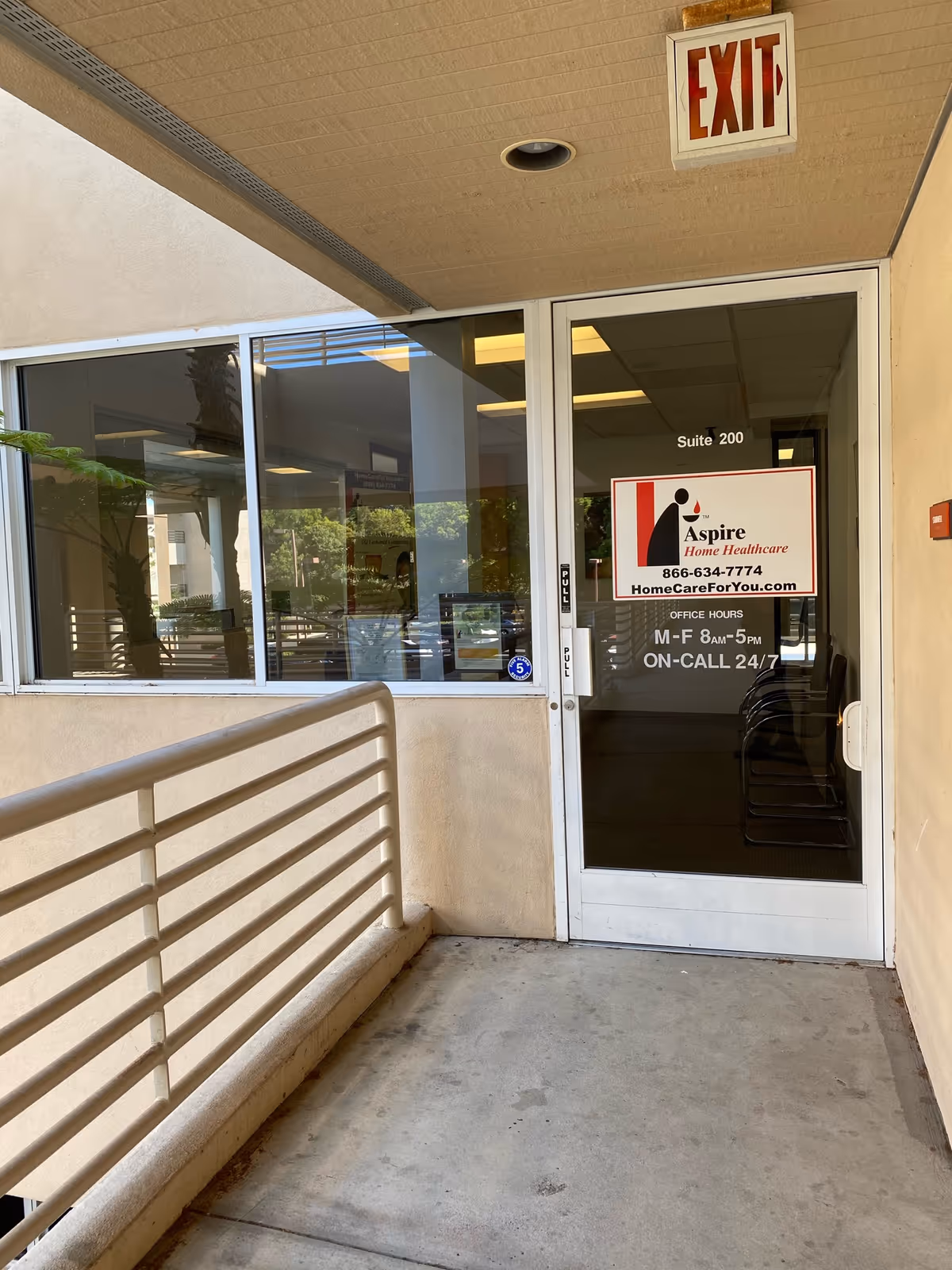 Exterior view of Aspire Home Healthcare entrance with glass door, exit sign, and railing.