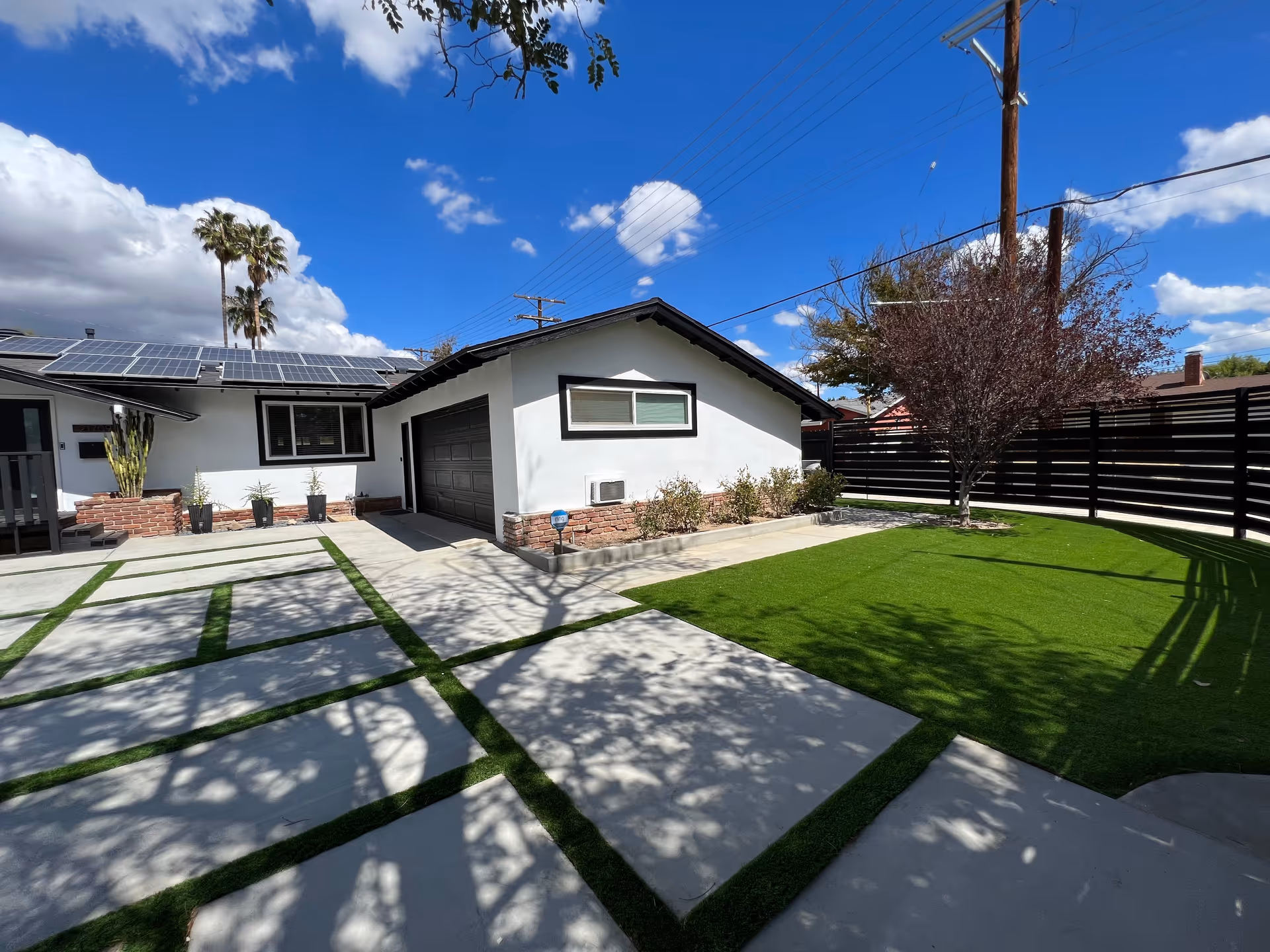 Modern single-story residence-style building with solar panels, a manicured yard, and a wooden fence.