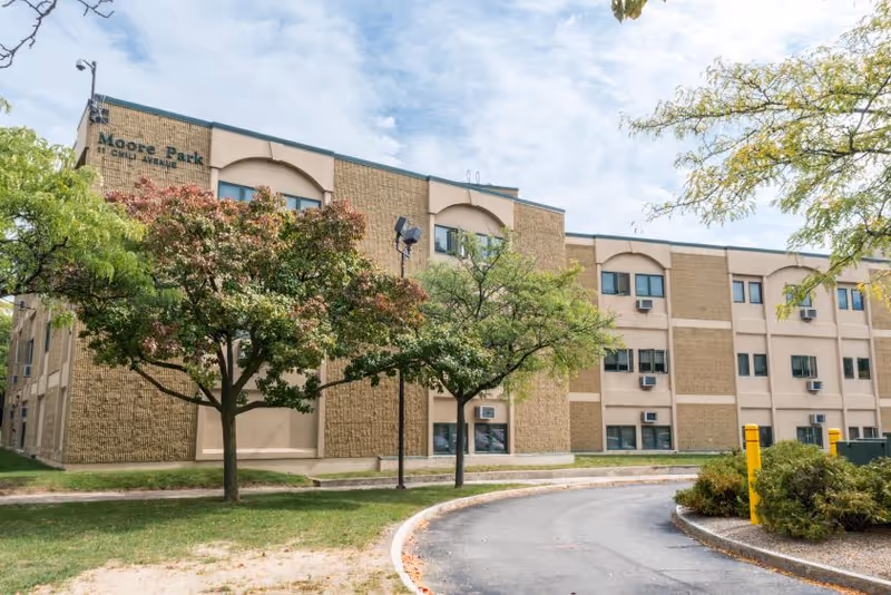 Exterior view of RRH Moore Park Senior Living building with trees and curved driveway.
