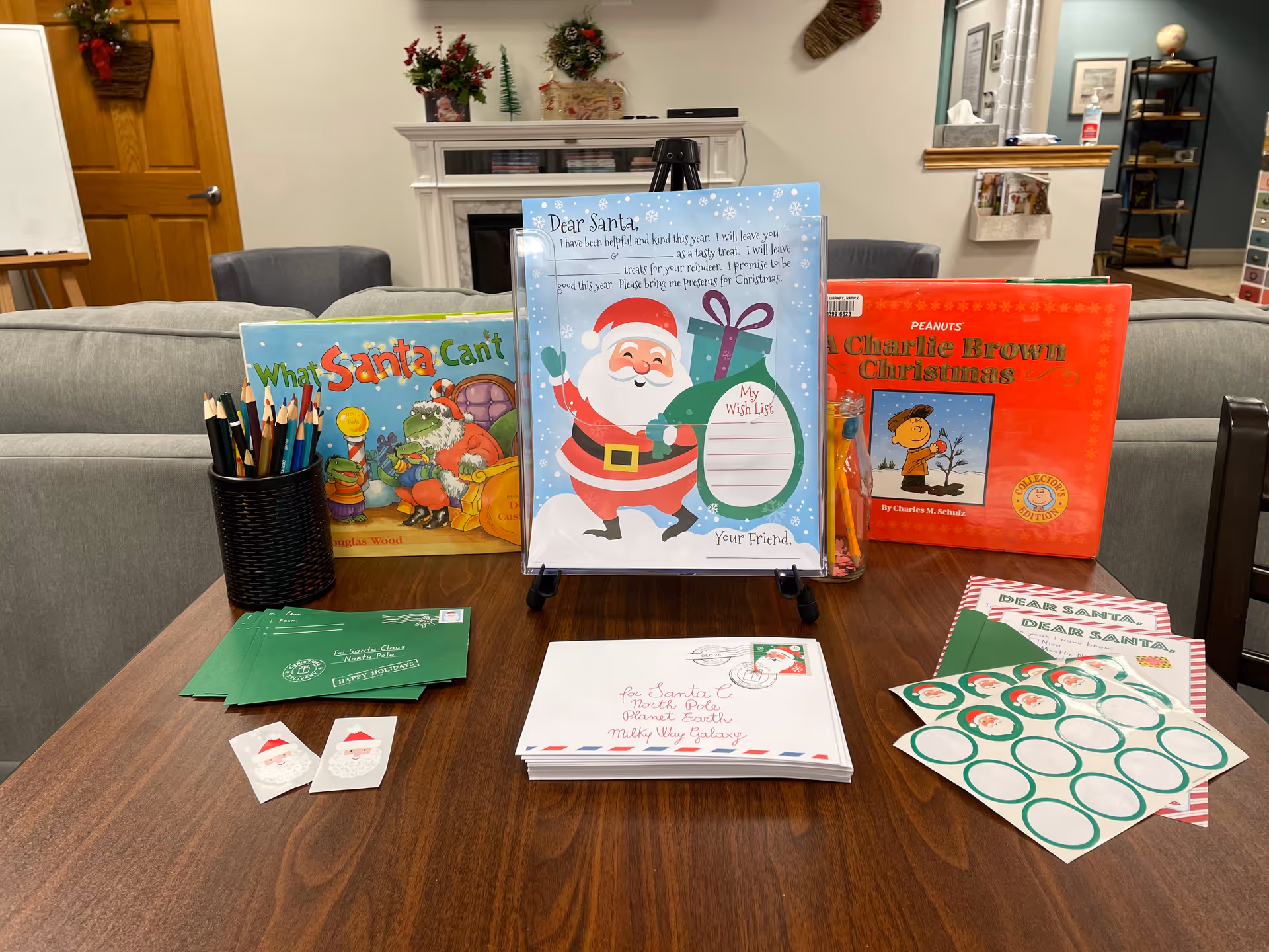 Table with holiday-themed books, envelopes, and crafts in a cozy living room.