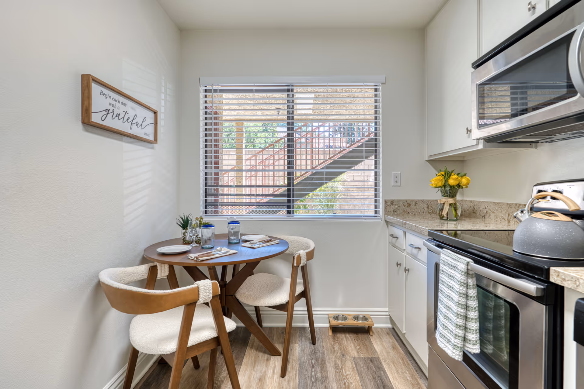 Cozy dining nook with round table, two chairs, and a window overlooking exterior stairs.
