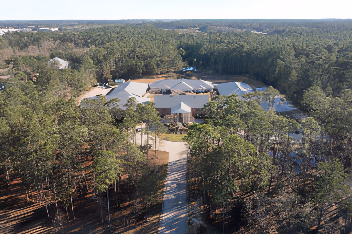 Aerial view of SummerHouse Park Provence facility surrounded by dense forest and greenery, with a long driveway leading up to the building complex.