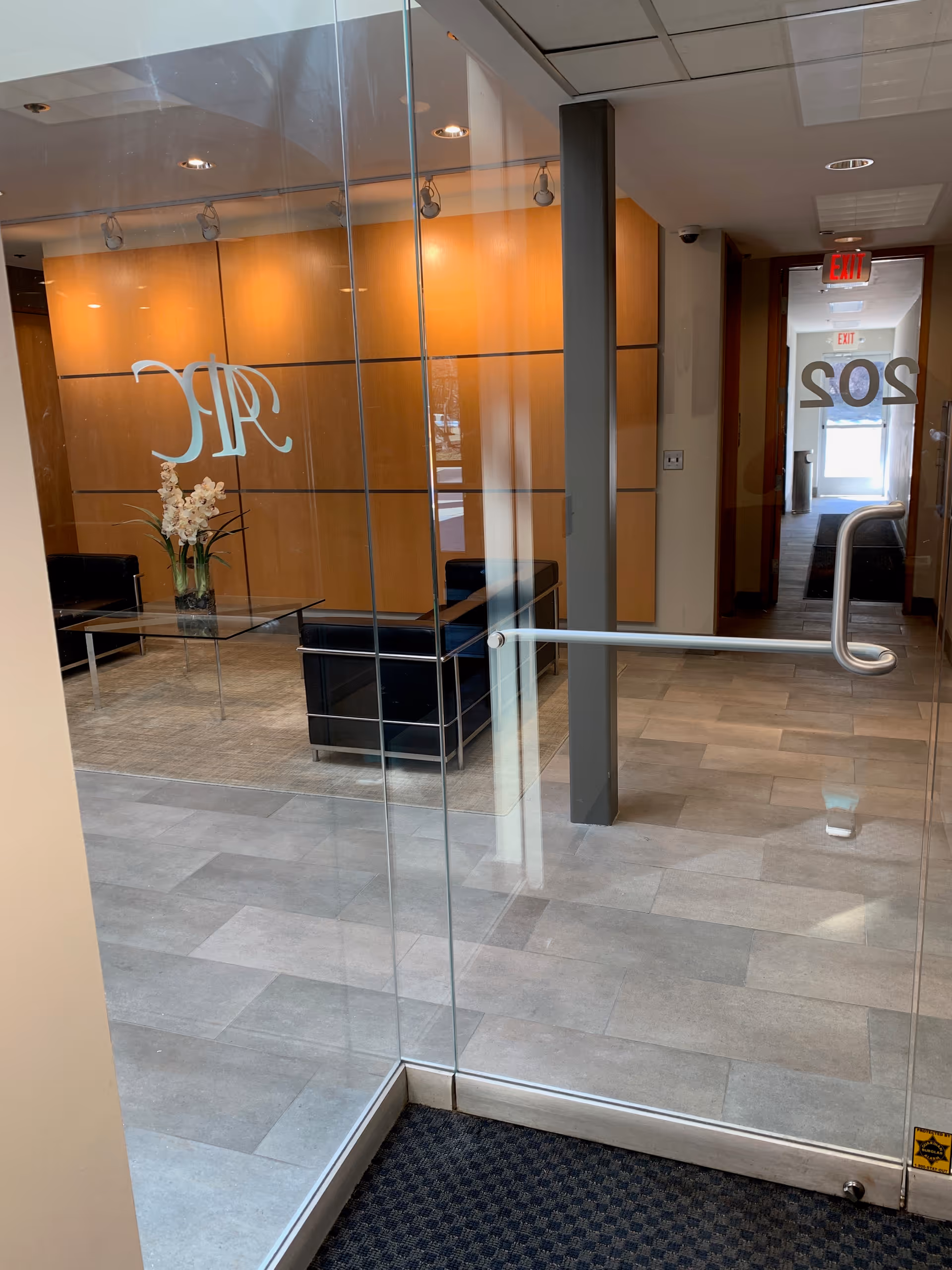 Glass-walled lobby with seating, a glass table with flowers, and a hallway.
