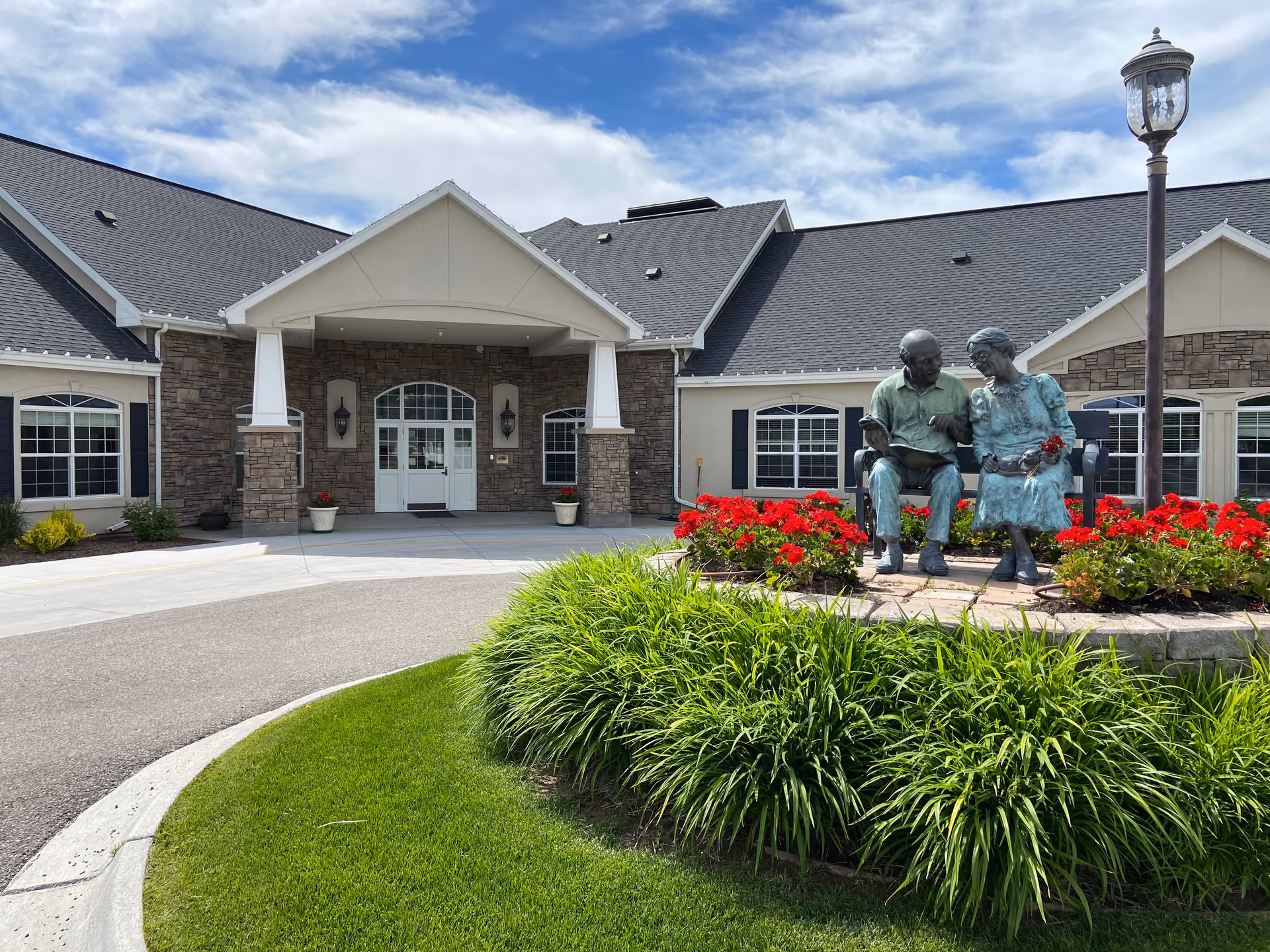 Front entrance of a senior living facility with a statue garden and red flowers.