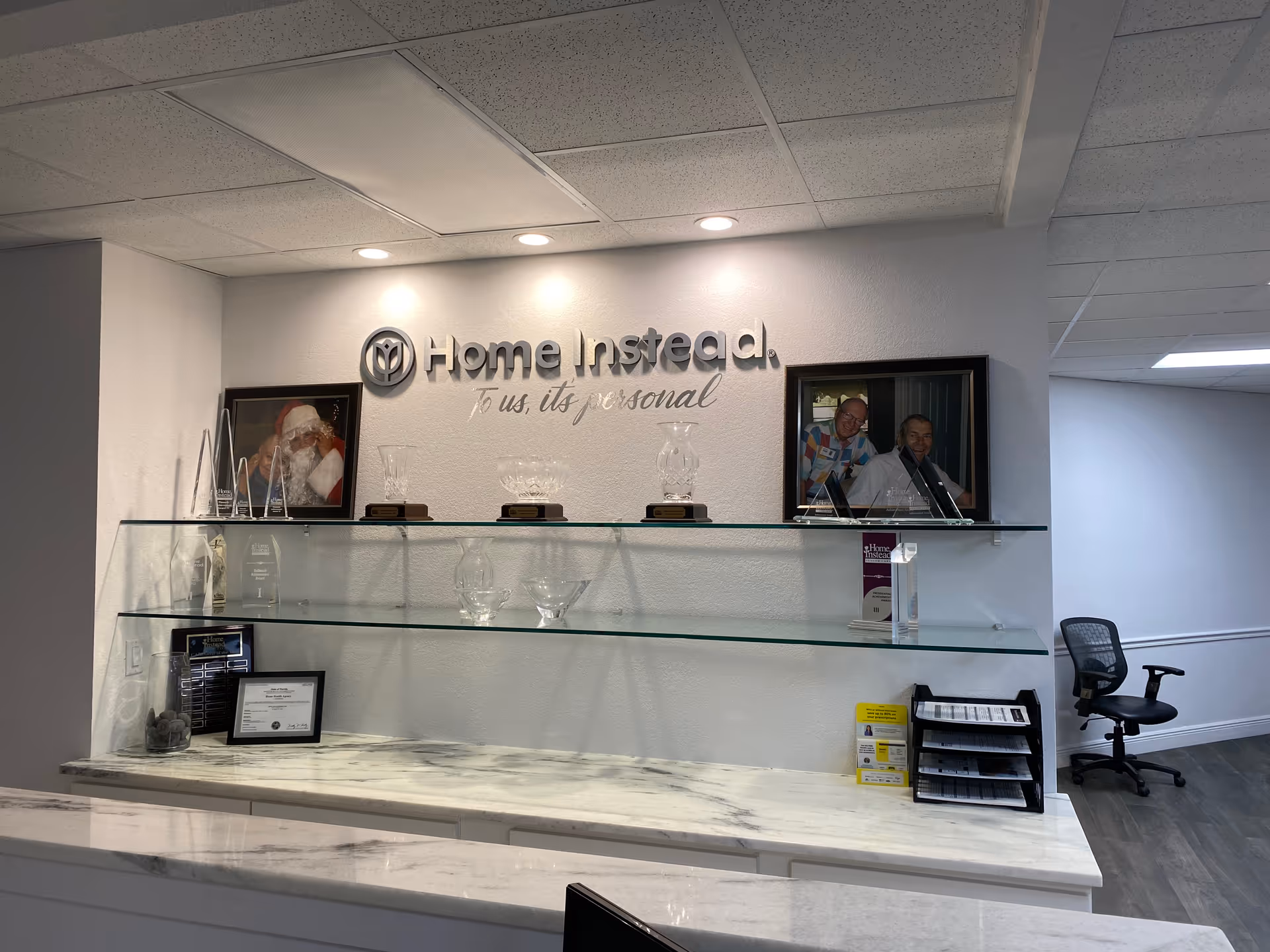 Reception area with Home Instead sign, glass shelves, awards, and photos.