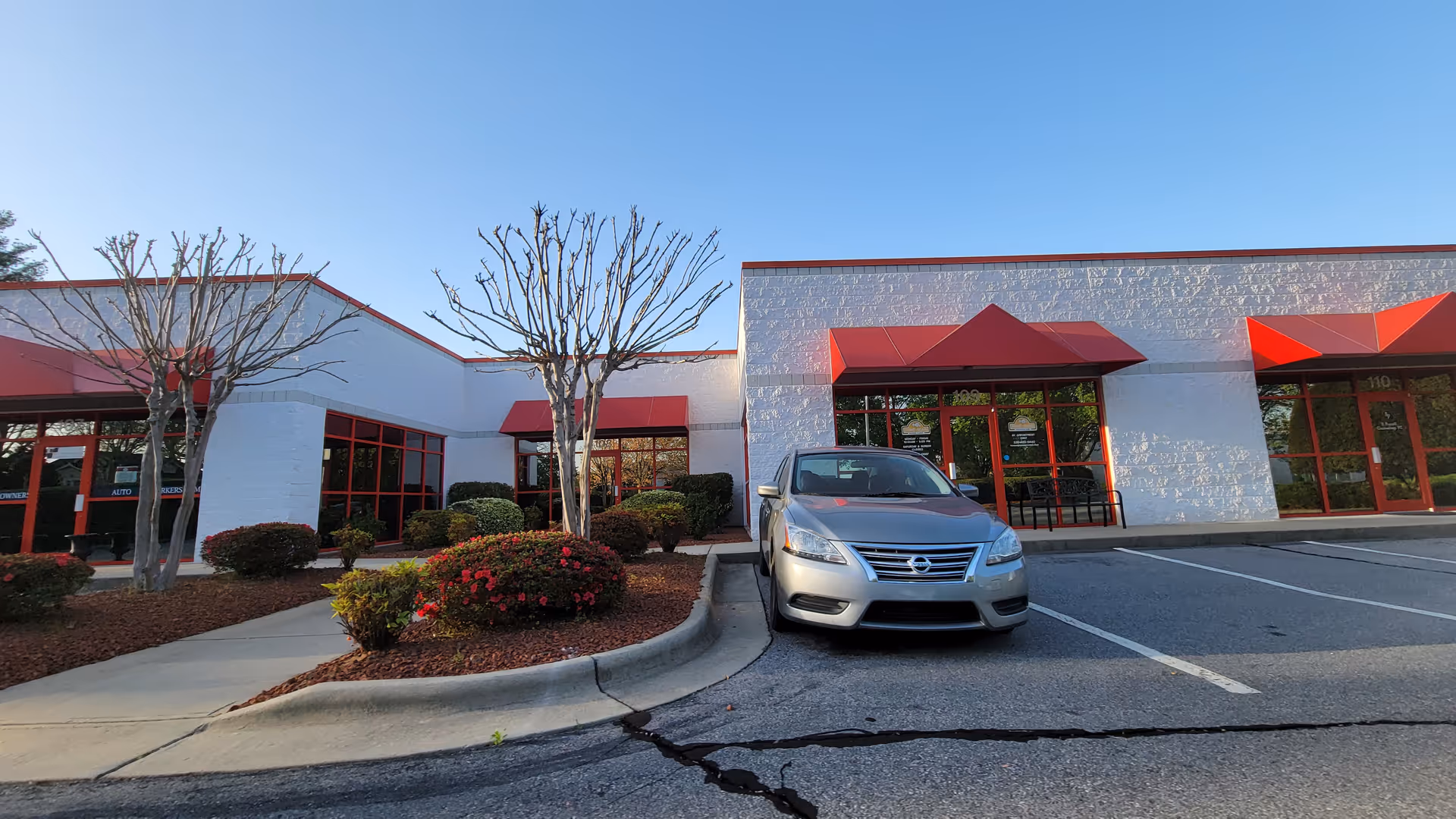 Exterior view of a commercial building with red awnings and a silver car in parking lot.