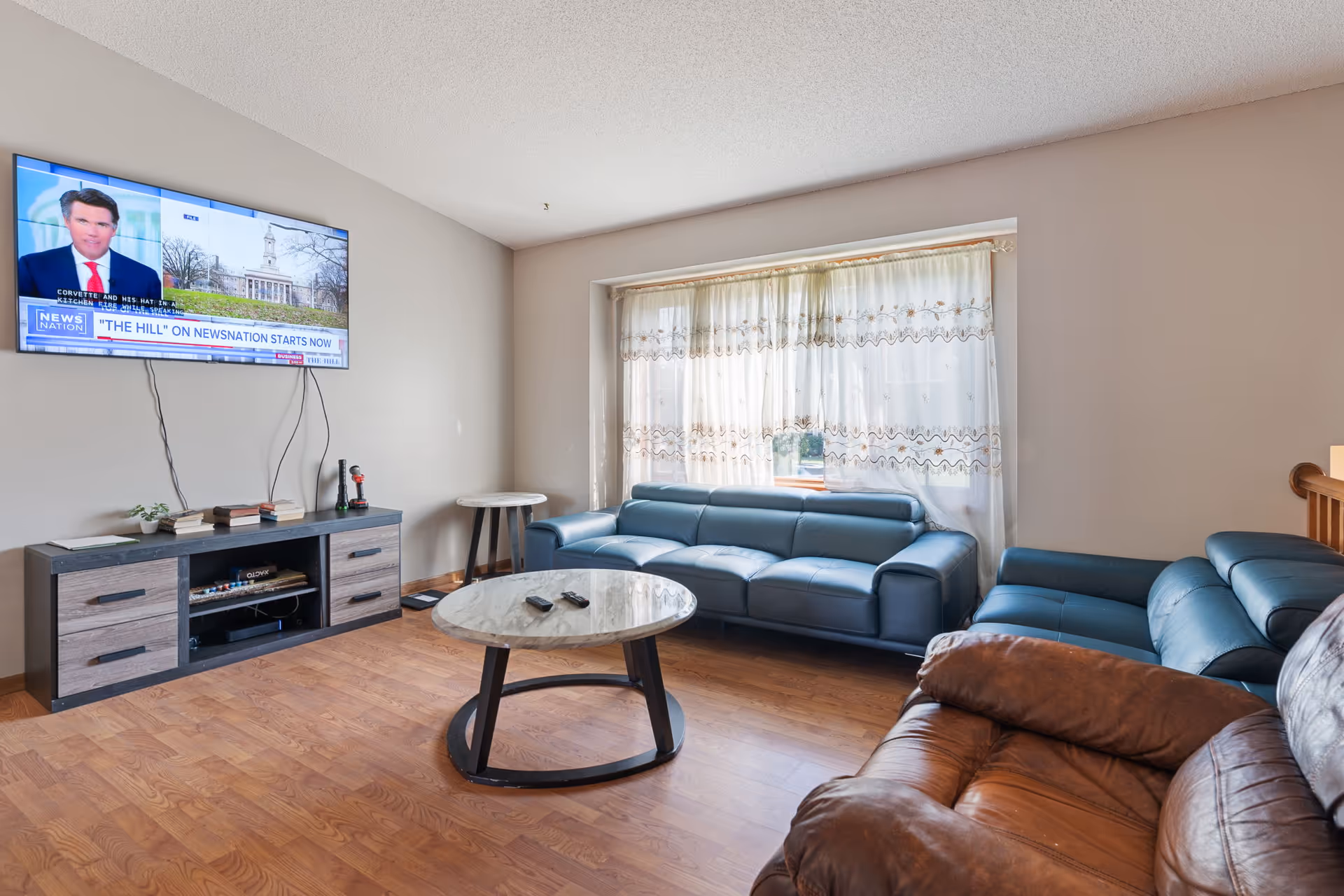 Living room with blue leather sofas, a marble coffee table, and a wall-mounted TV.