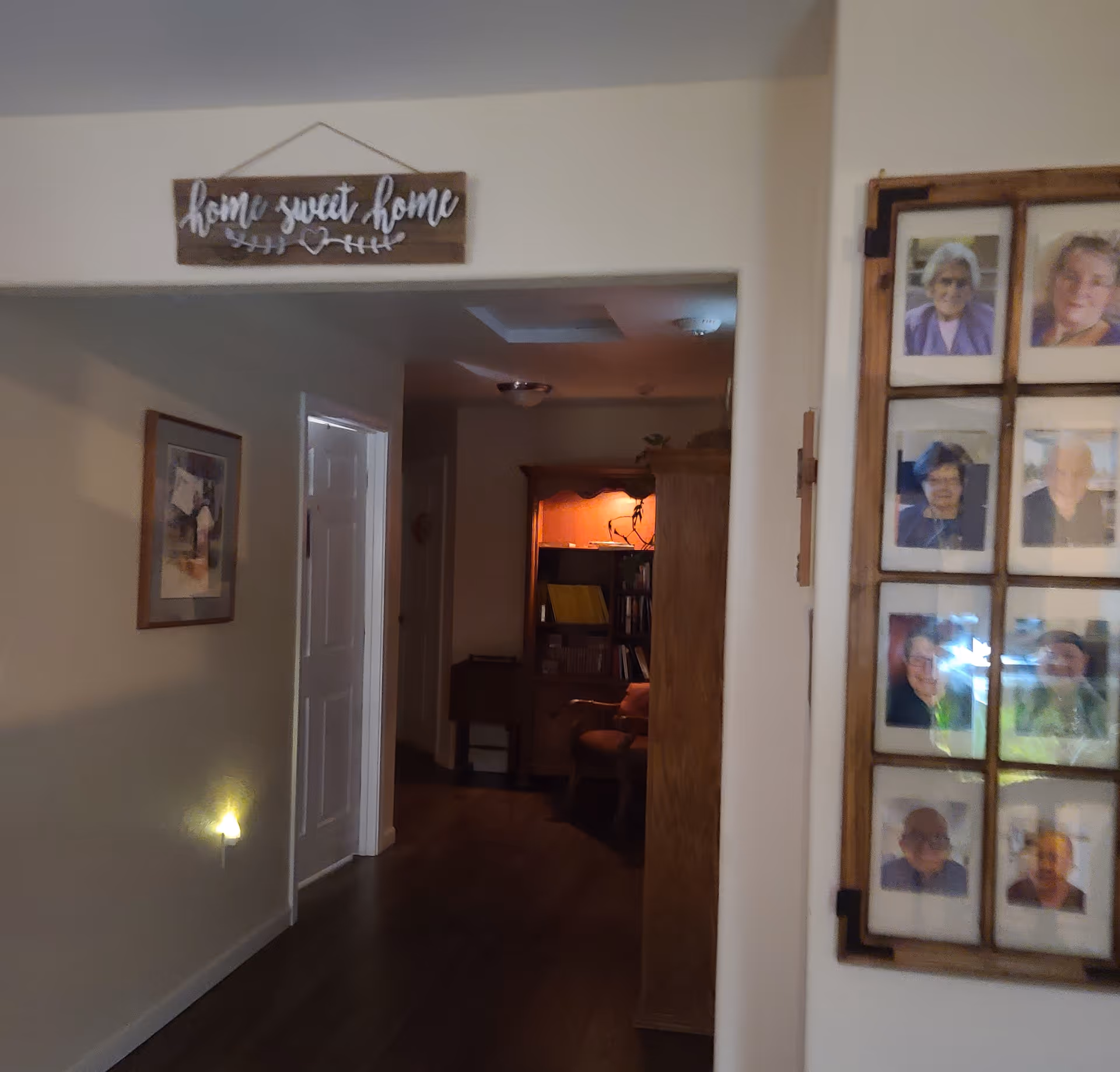 Hallway of a senior living facility with photo collage and warm lighting toward a cozy room.