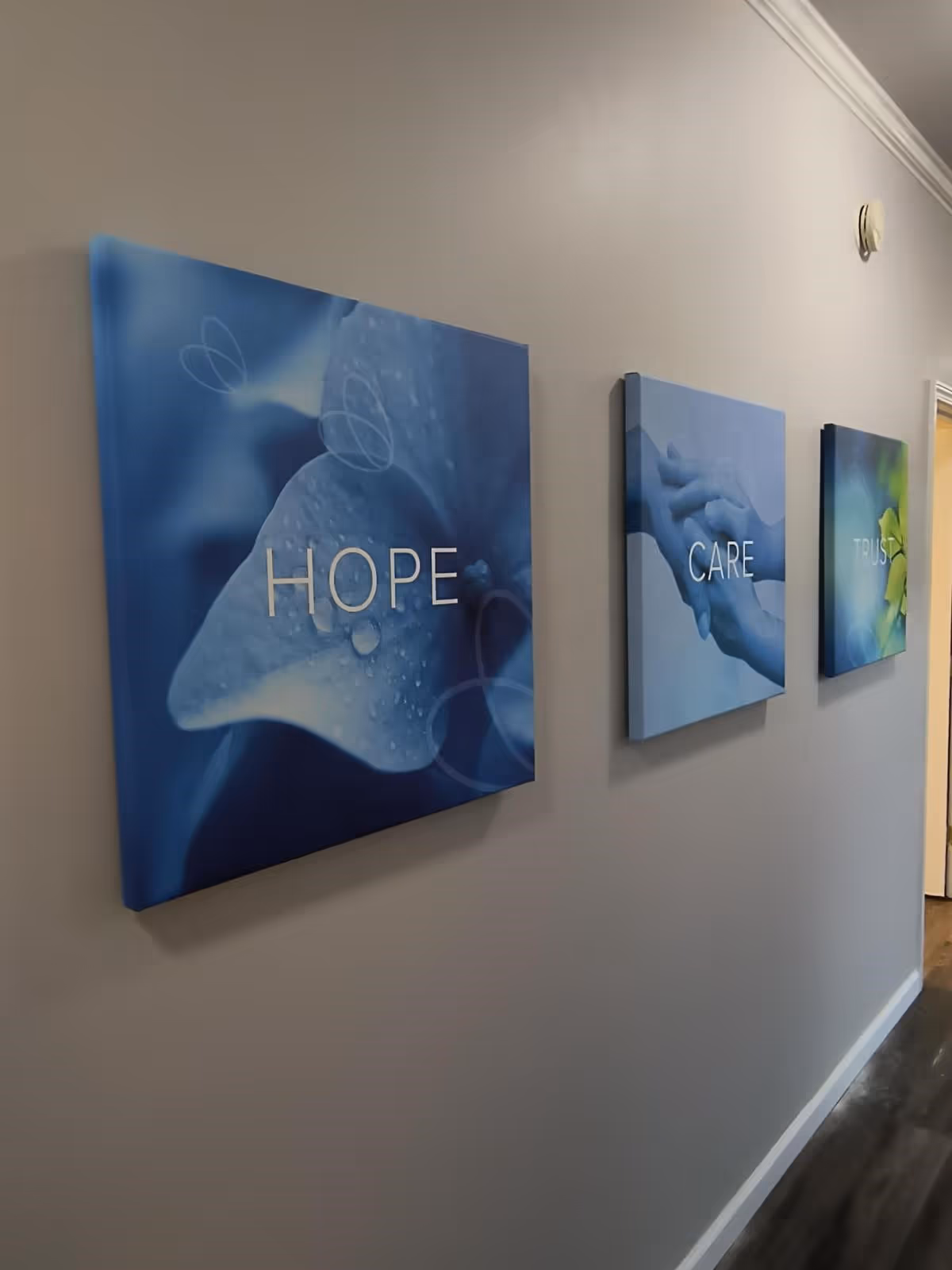 Blue hallway wall displays three canvases reading HOPE, CARE, and TRUST.