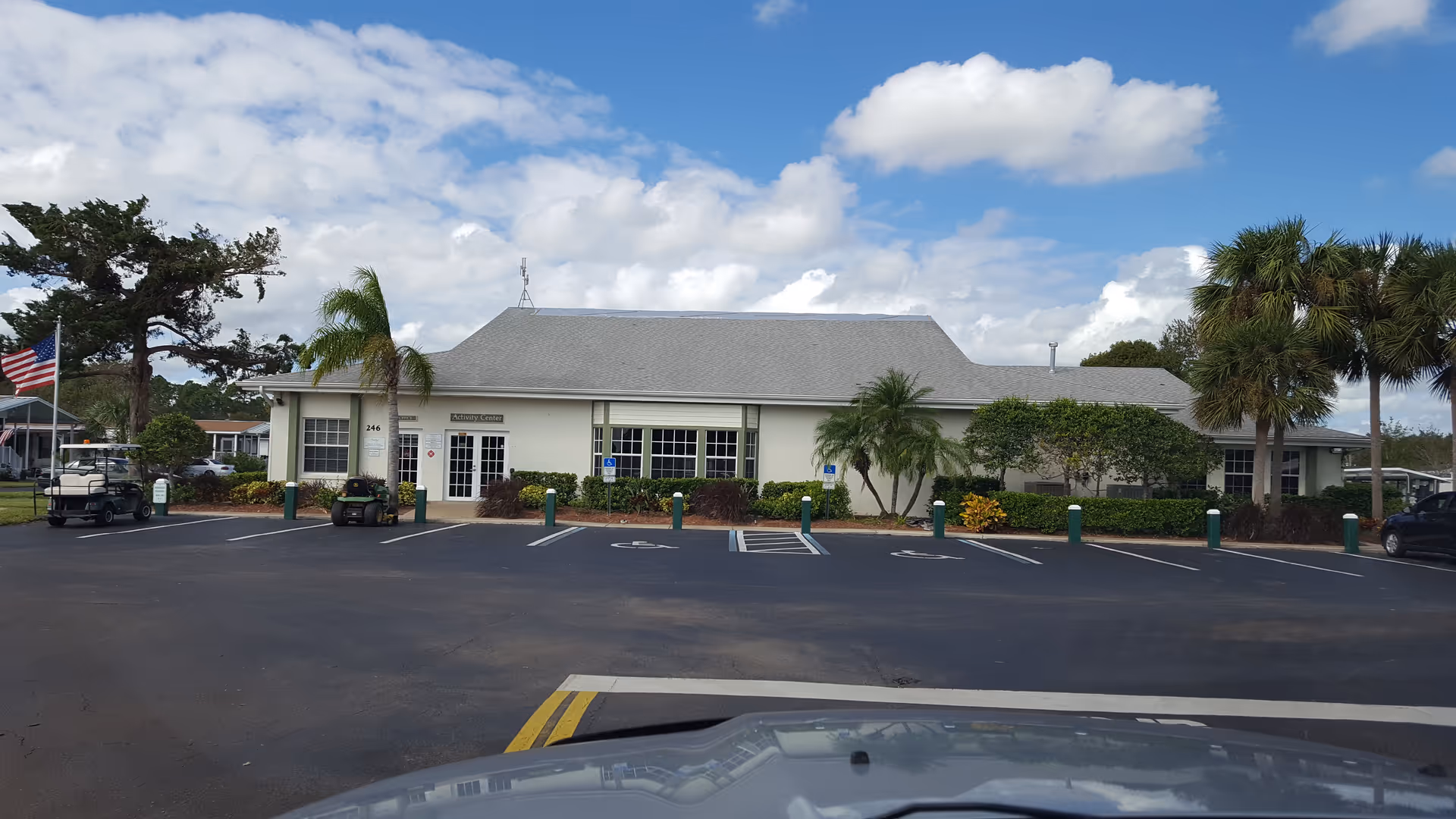 Single-story nursing facility with gray roof, parking lot, palm trees, and American flag.