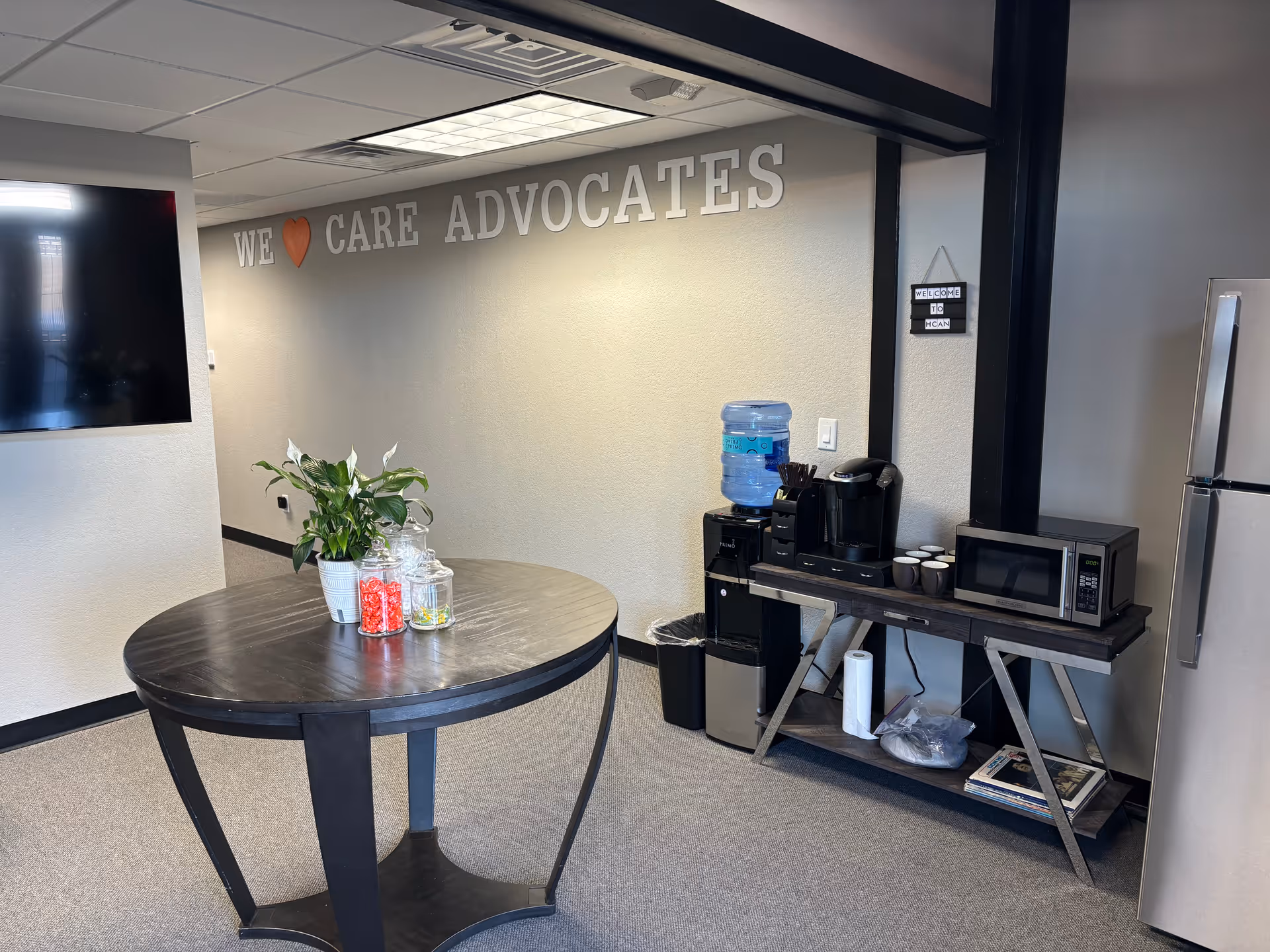 Interior break room with round table, plant, candy jars, and beverage station.