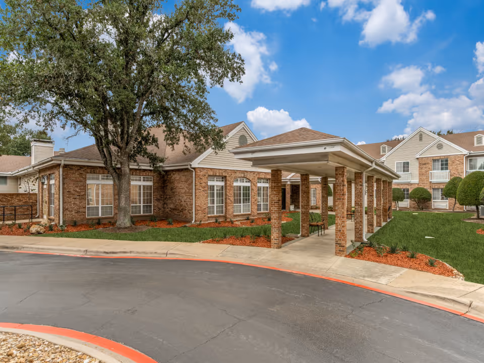 Brick senior living facility exterior with a covered entrance and manicured landscaping.