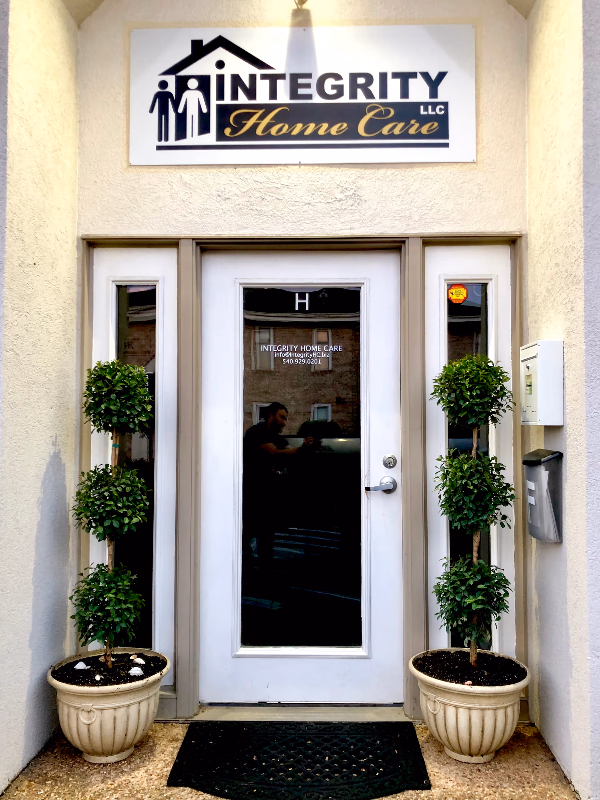 Front entrance of Integrity Home Care LLC with glass door and two potted topiary plants.