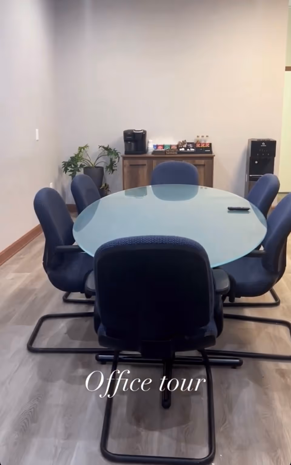 Round glass conference table with blue chairs in a small office area.