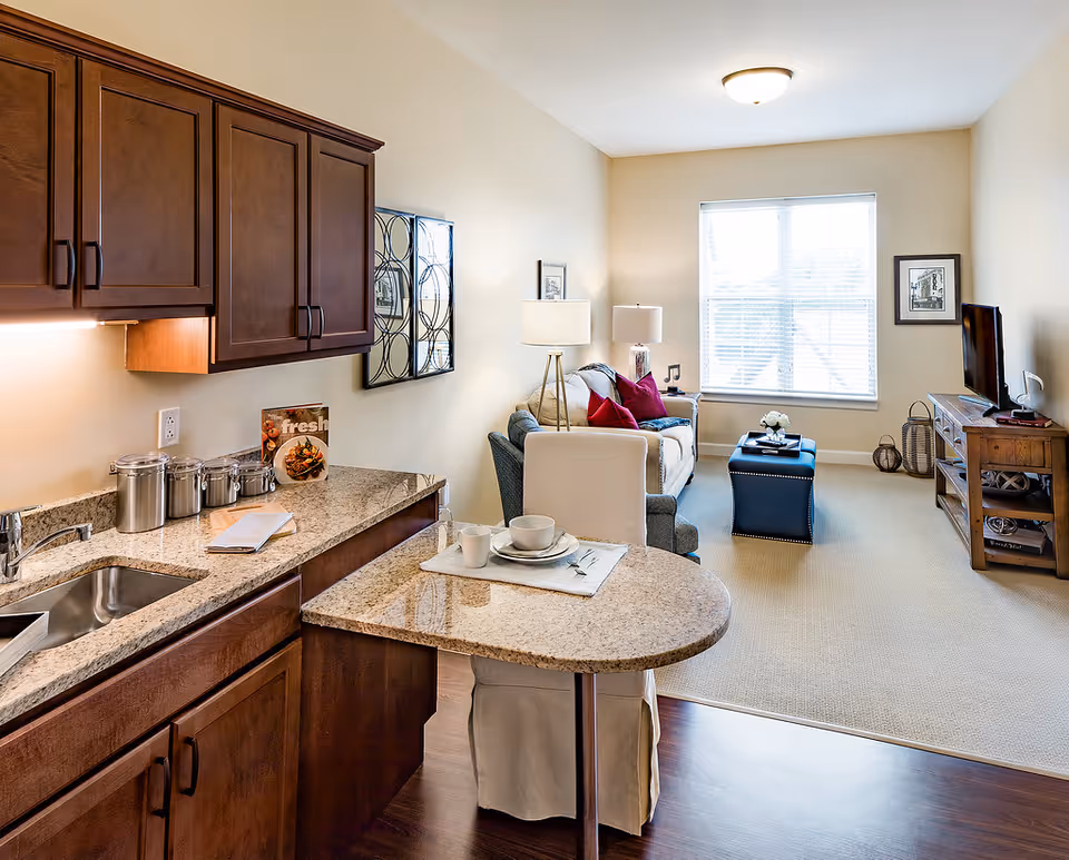 Open, well-lit living area with kitchen counter, sofa, coffee table, and TV.