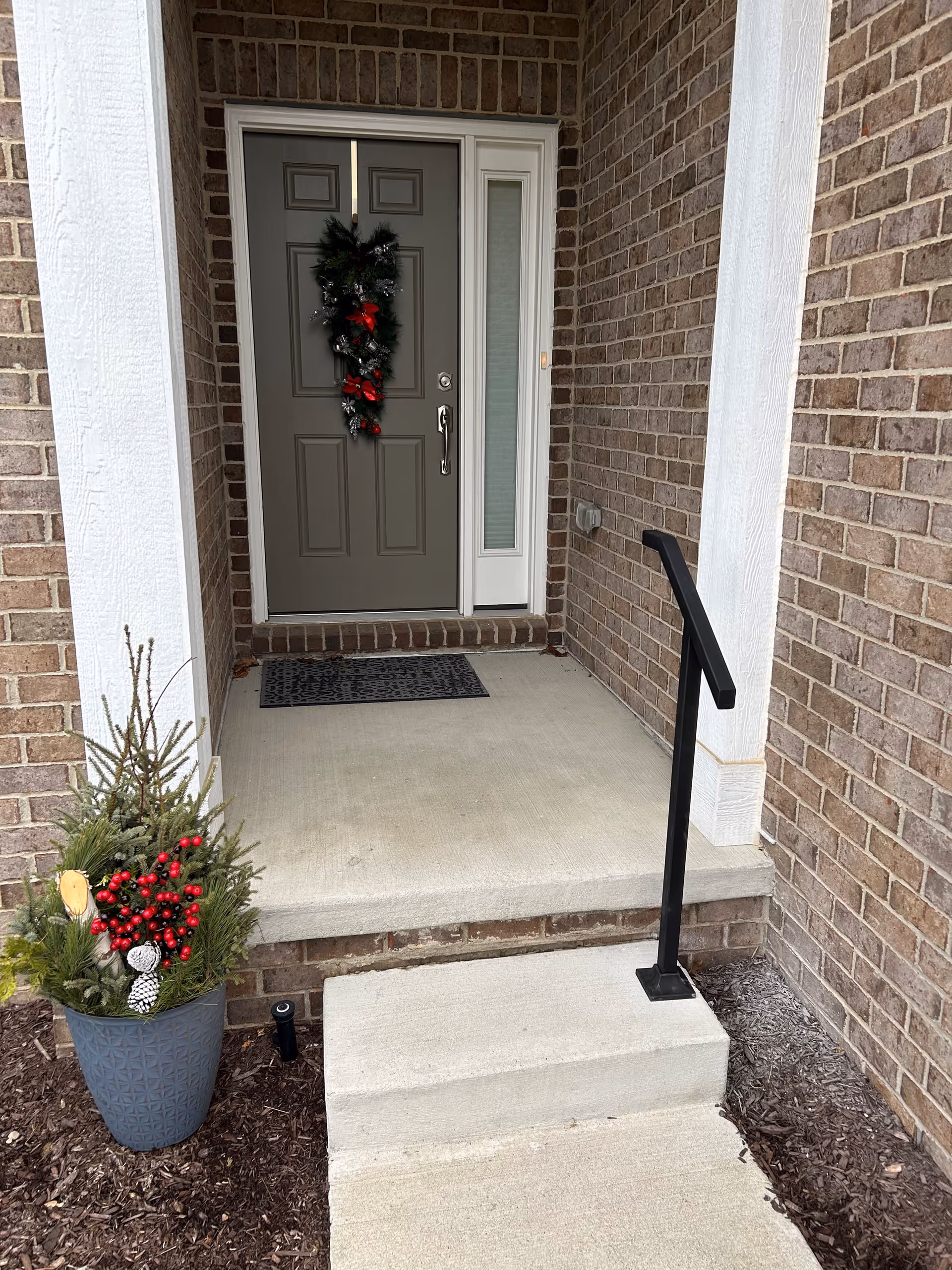 Brick exterior entry with a wreath on the door, a concrete porch, and planters.