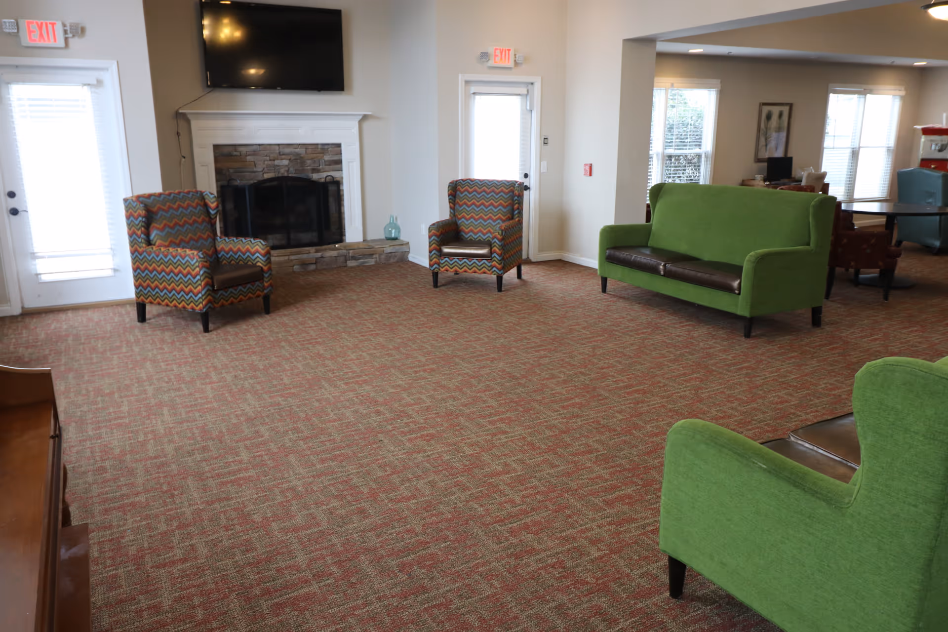 Spacious living room with green couches, colorful chairs, and a fireplace.