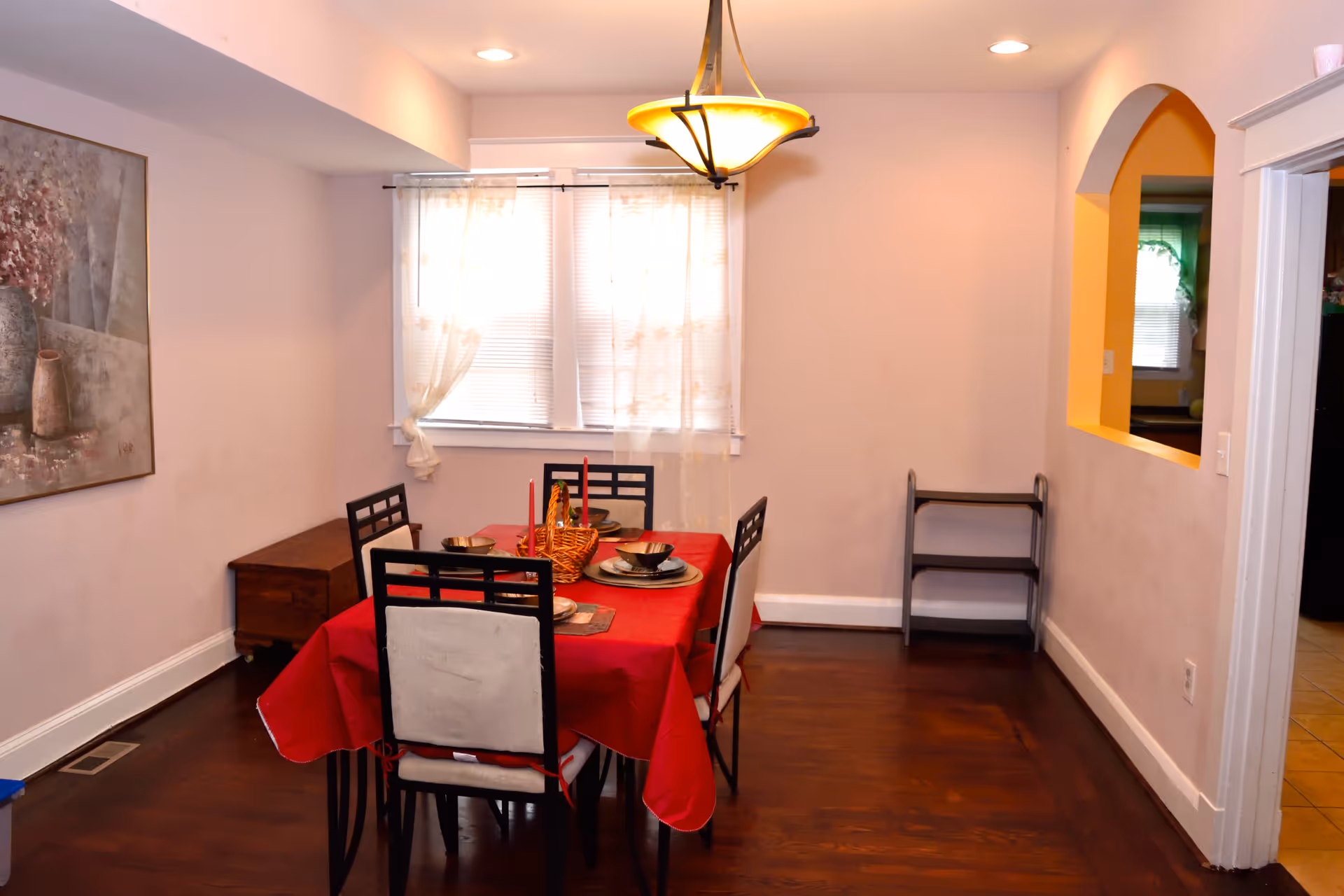 Dining room with red tablecloth, chairs, chandelier, and window.