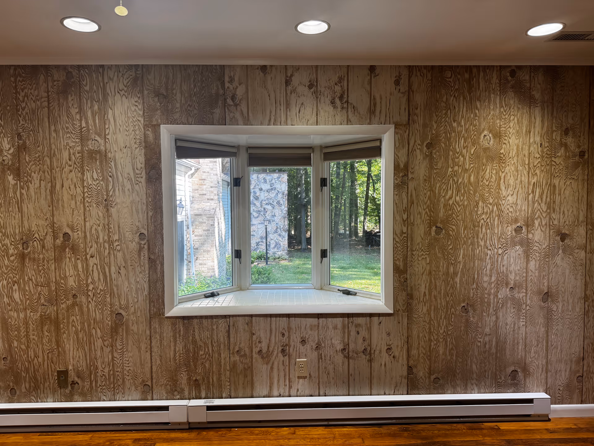 Wood-paneled interior wall featuring a bay window looking out to greenery